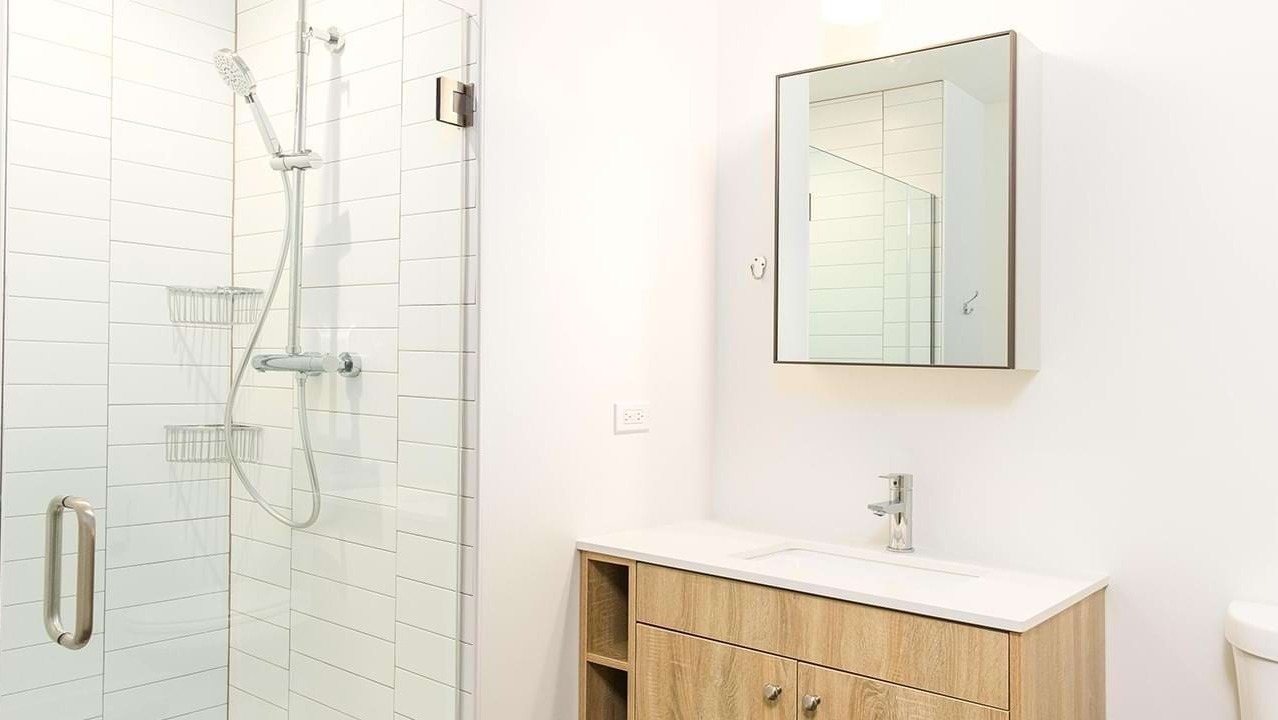 Contemporary bathroom with a sleek vanity, mirror, and a spacious walk-in shower featuring subway tiles at The Duncan apartments in Chicago