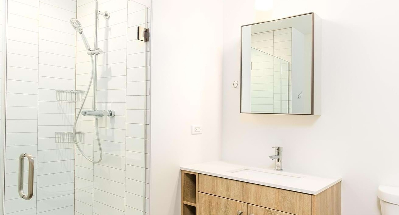 Contemporary bathroom with a sleek vanity, mirror, and a spacious walk-in shower featuring subway tiles at The Duncan apartments in Chicago