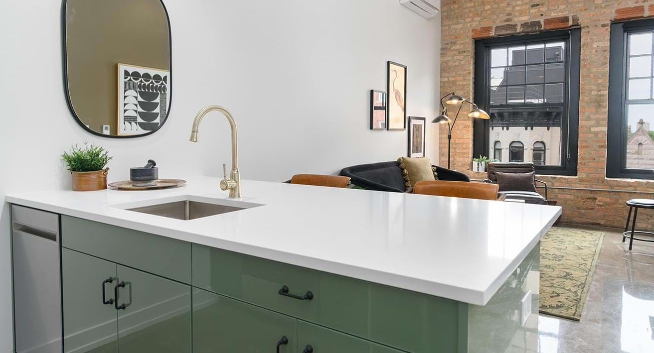 Open-concept apartment featuring a modern kitchen island with green cabinets, integrating seamlessly into the living space at The Duncan in Chicago