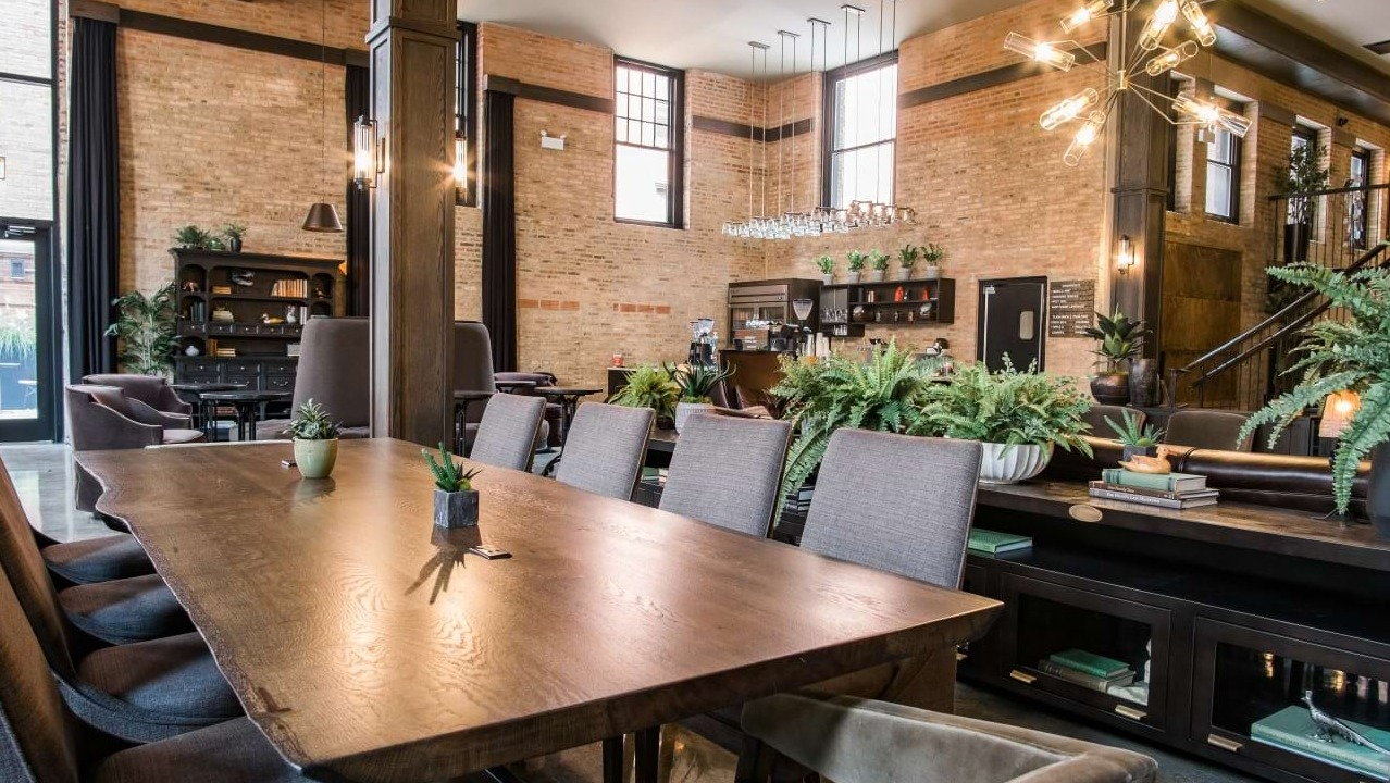 Elegant resident dining room with a long communal table, exposed brick walls, and modern lighting fixtures at The Duncan in Chicago