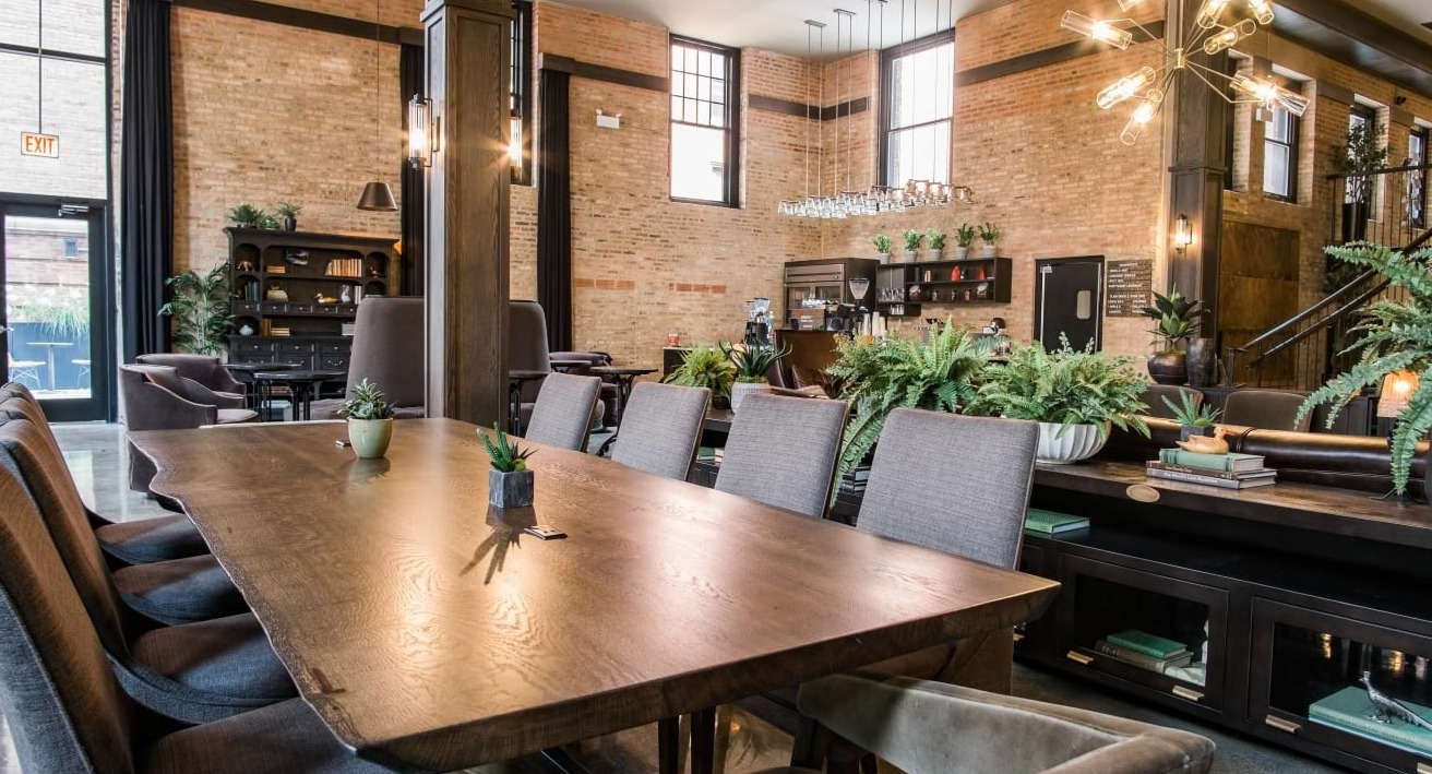 Elegant resident dining room with a long communal table, exposed brick walls, and modern lighting fixtures at The Duncan in Chicago
