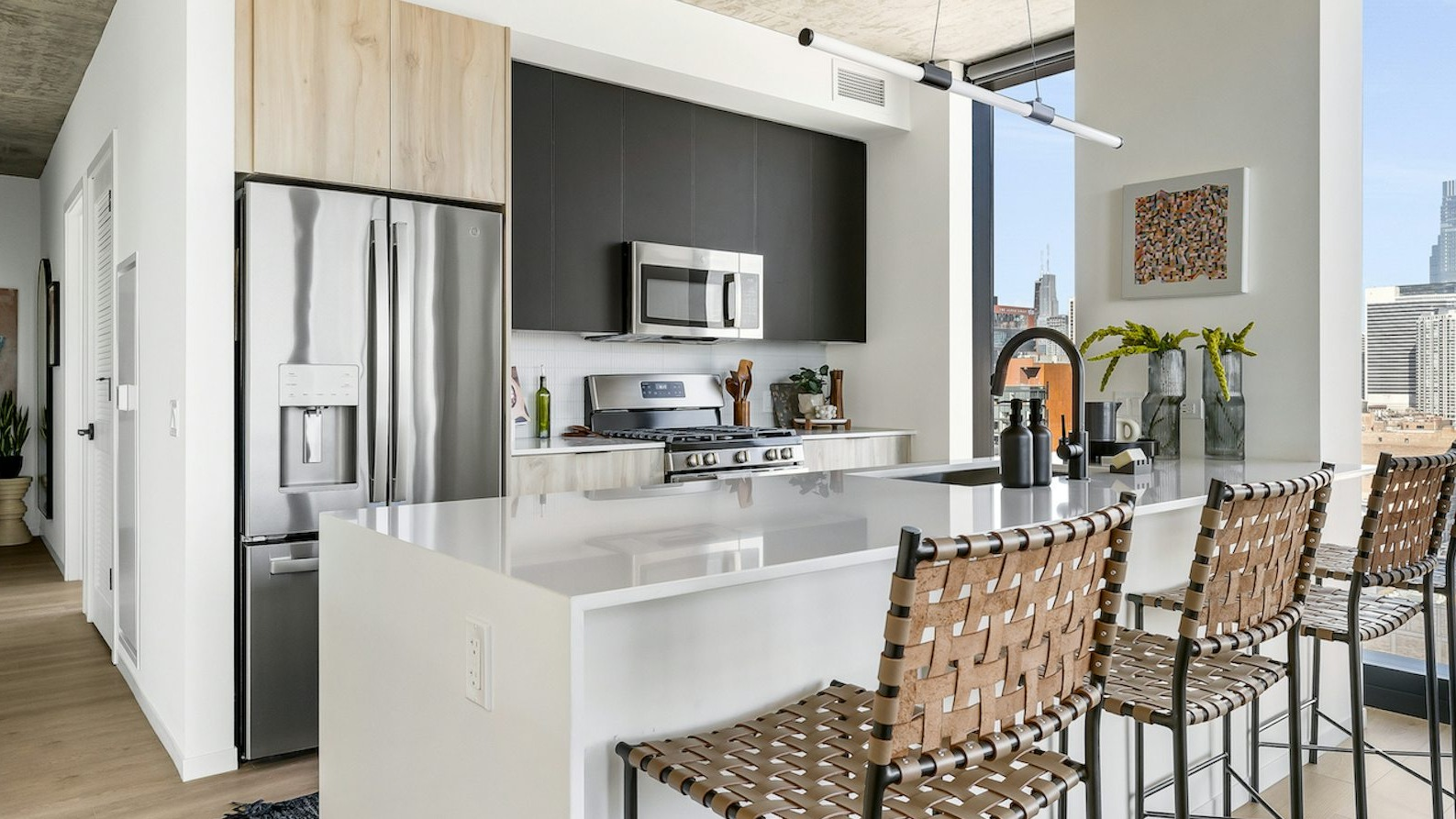 Luxury apartment kitchen featuring a large island, stainless steel appliances, and panoramic city views from floor-to-ceiling windows at The Dylan in Chicago