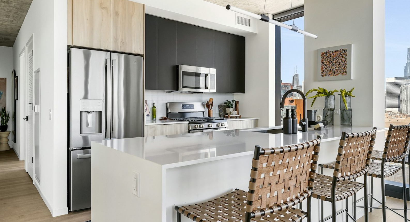 Luxury apartment kitchen featuring a large island, stainless steel appliances, and panoramic city views from floor-to-ceiling windows at The Dylan in Chicago