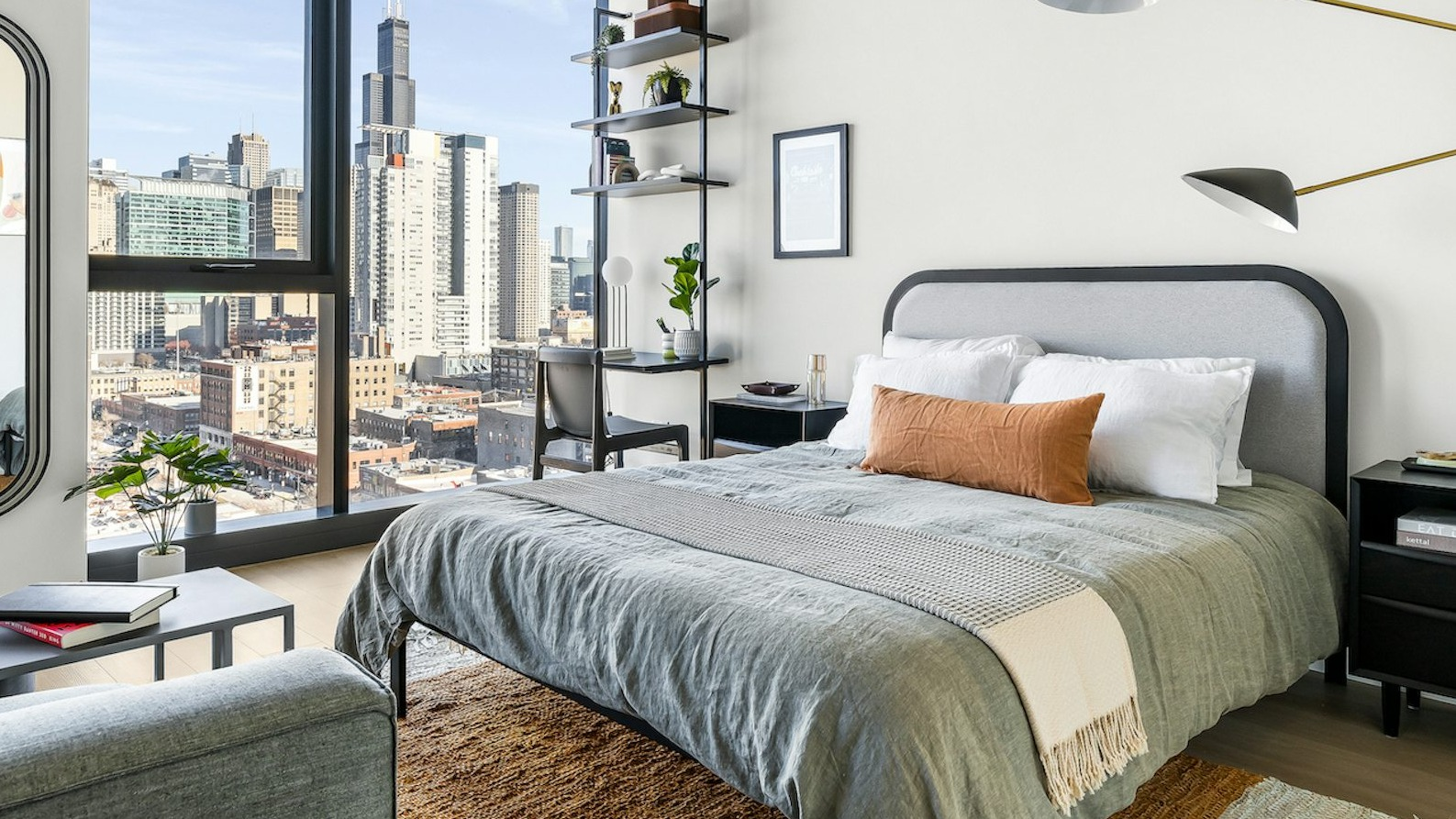 Contemporary bedroom with a comfortable bed, stylish lighting, desk, and large windows revealing breathtaking city views at The Dylan in Chicago