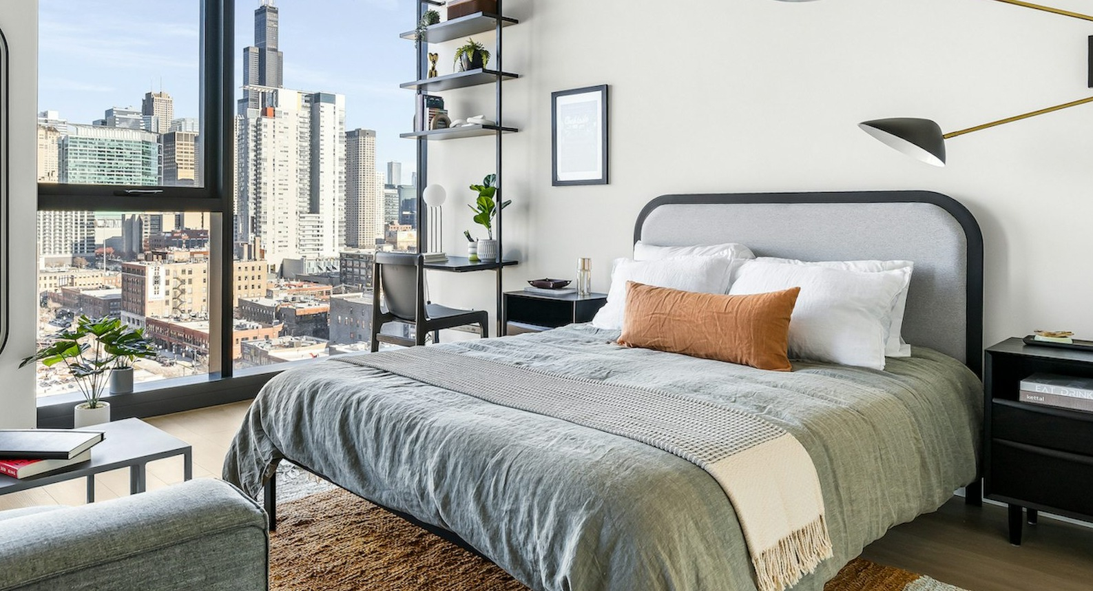 Contemporary bedroom with a comfortable bed, stylish lighting, desk, and large windows revealing breathtaking city views at The Dylan in Chicago
