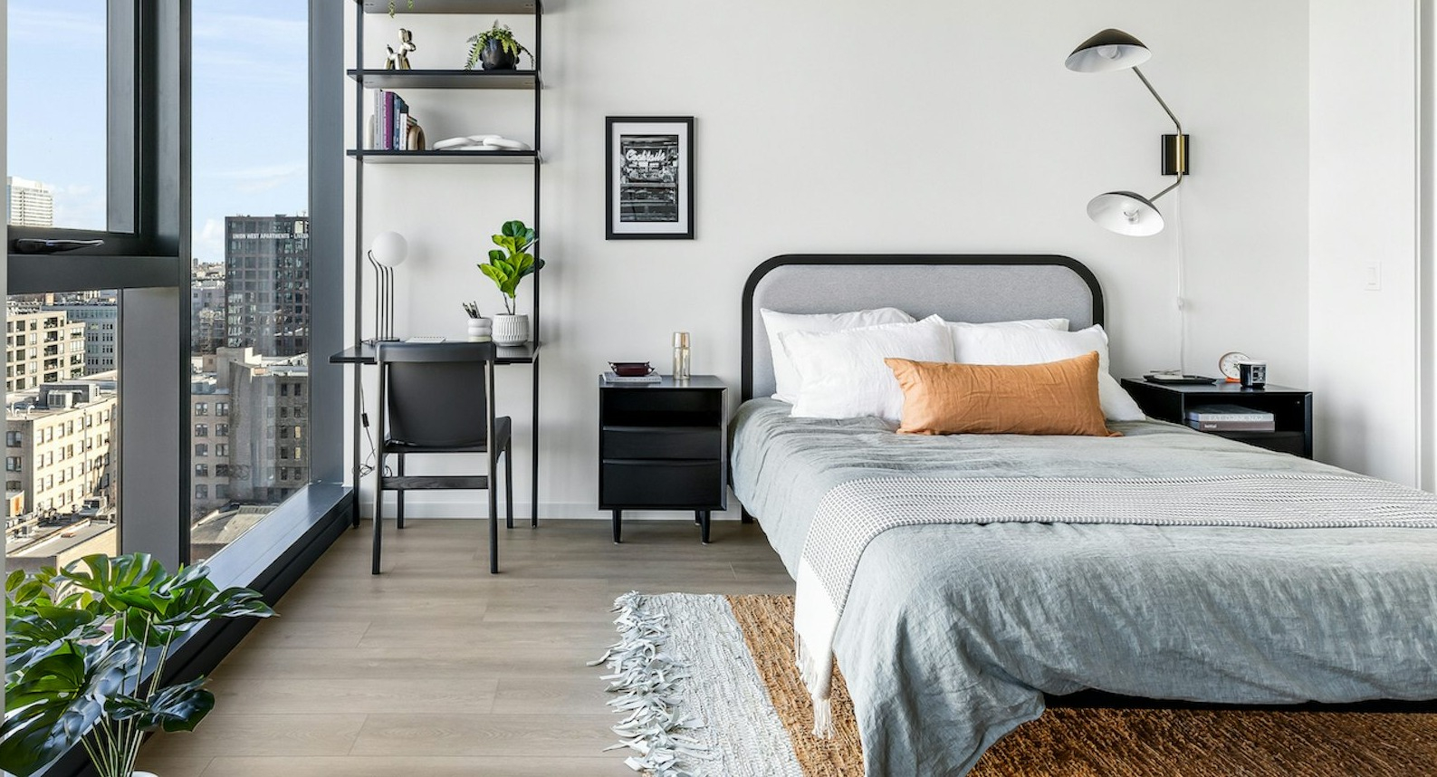 Contemporary bedroom featuring a comfortable bed, functional workspace with shelving, and large windows offering expansive city views at The Dylan in Chicago