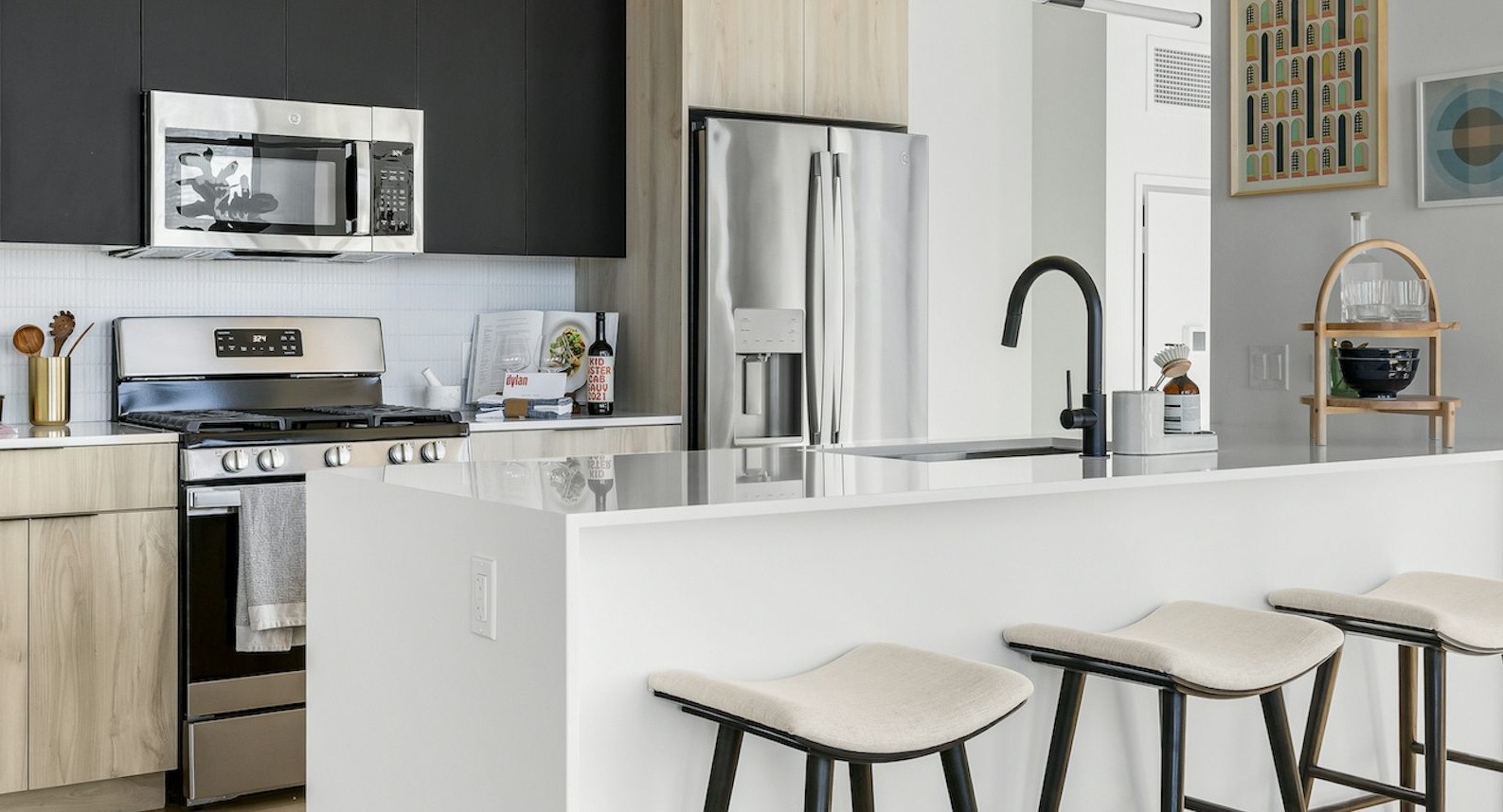 Sleek modern kitchen with two-toned cabinetry, stainless steel appliances, a large island with bar stools, and artistic decor at The Dylan in Chicago