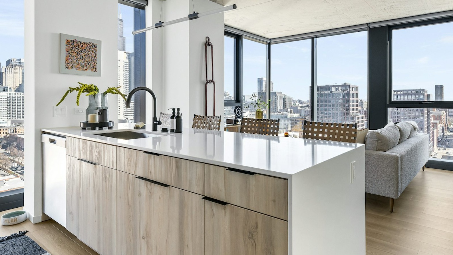 Open-concept living and dining area with a modern kitchen island, comfortable seating, and floor-to-ceiling windows showcasing city views at The Dylan in Chicago