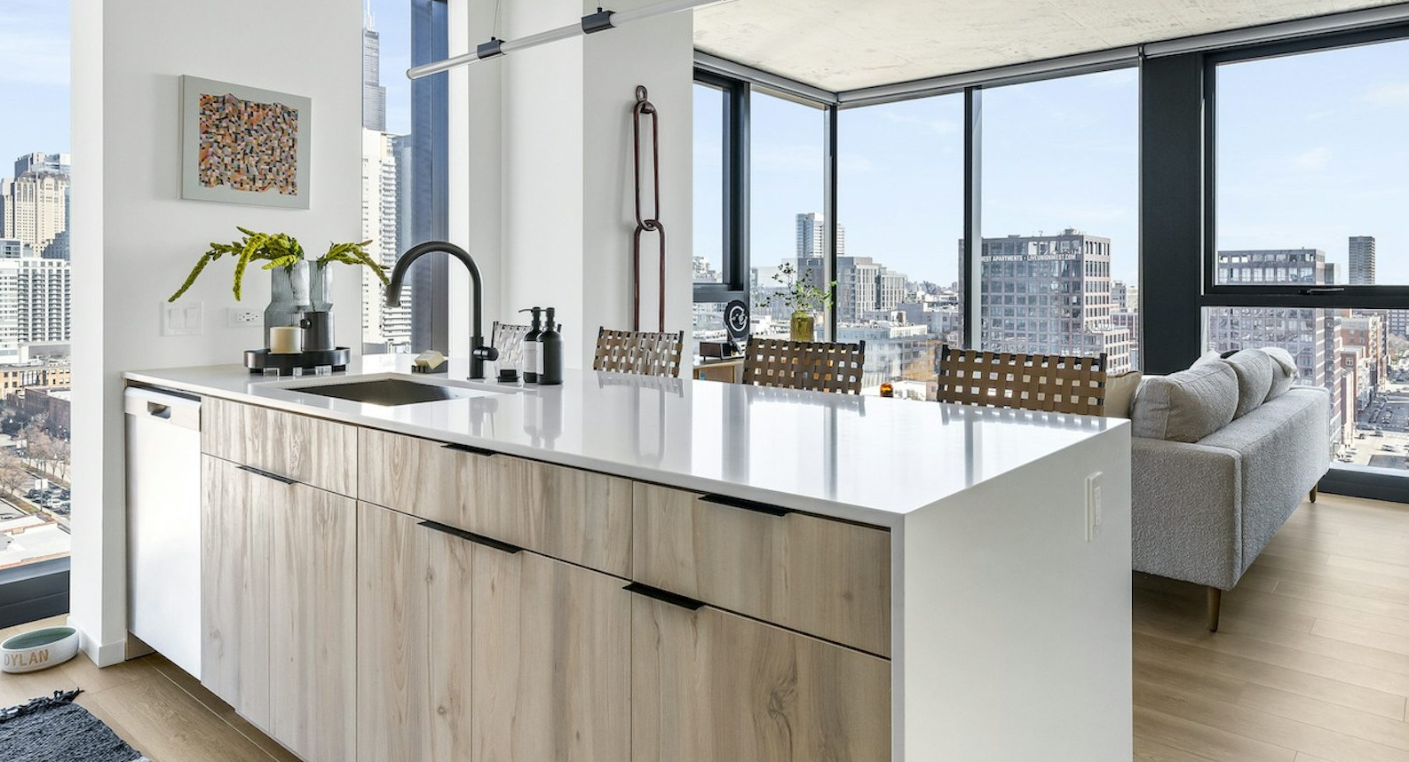 Open-concept living and dining area with a modern kitchen island, comfortable seating, and floor-to-ceiling windows showcasing city views at The Dylan in Chicago