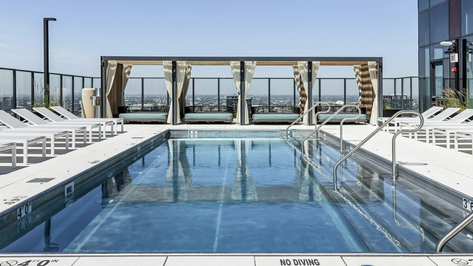 Inviting rooftop swimming pool surrounded by white lounge chairs and private cabanas, offering city views under a clear sky at The Dylan in Chicago