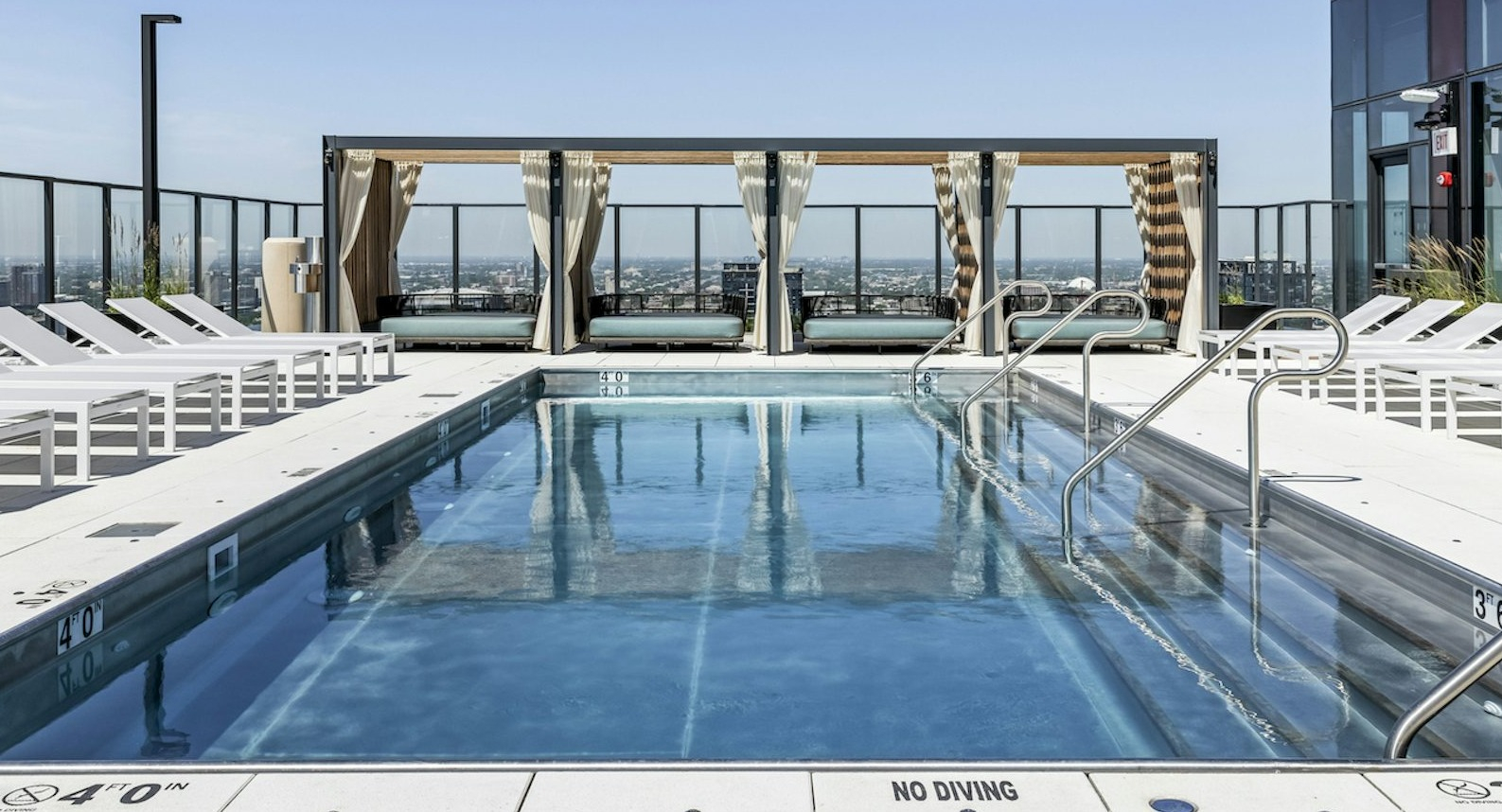 Inviting rooftop swimming pool surrounded by white lounge chairs and private cabanas, offering city views under a clear sky at The Dylan in Chicago
