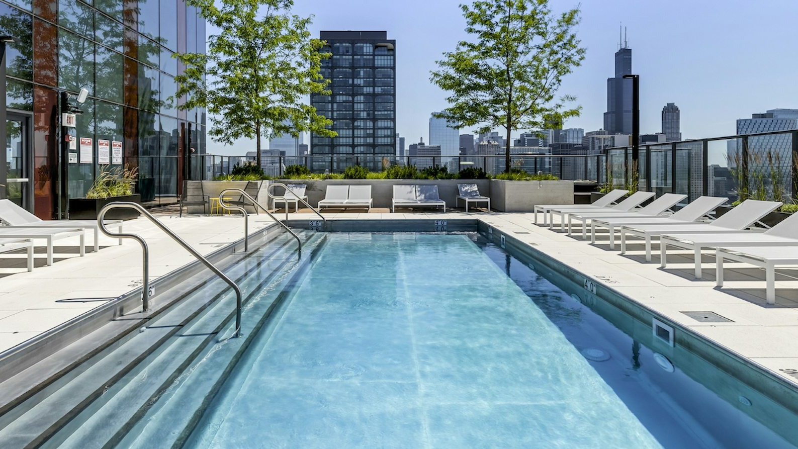 Modern rooftop pool surrounded by lounge chairs, offering stunning city skyline views, and lush greenery at The Dylan in Chicago