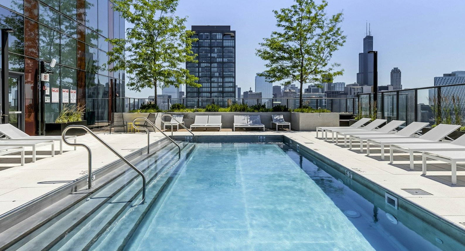 Modern rooftop pool surrounded by lounge chairs, offering stunning city skyline views, and lush greenery at The Dylan in Chicago