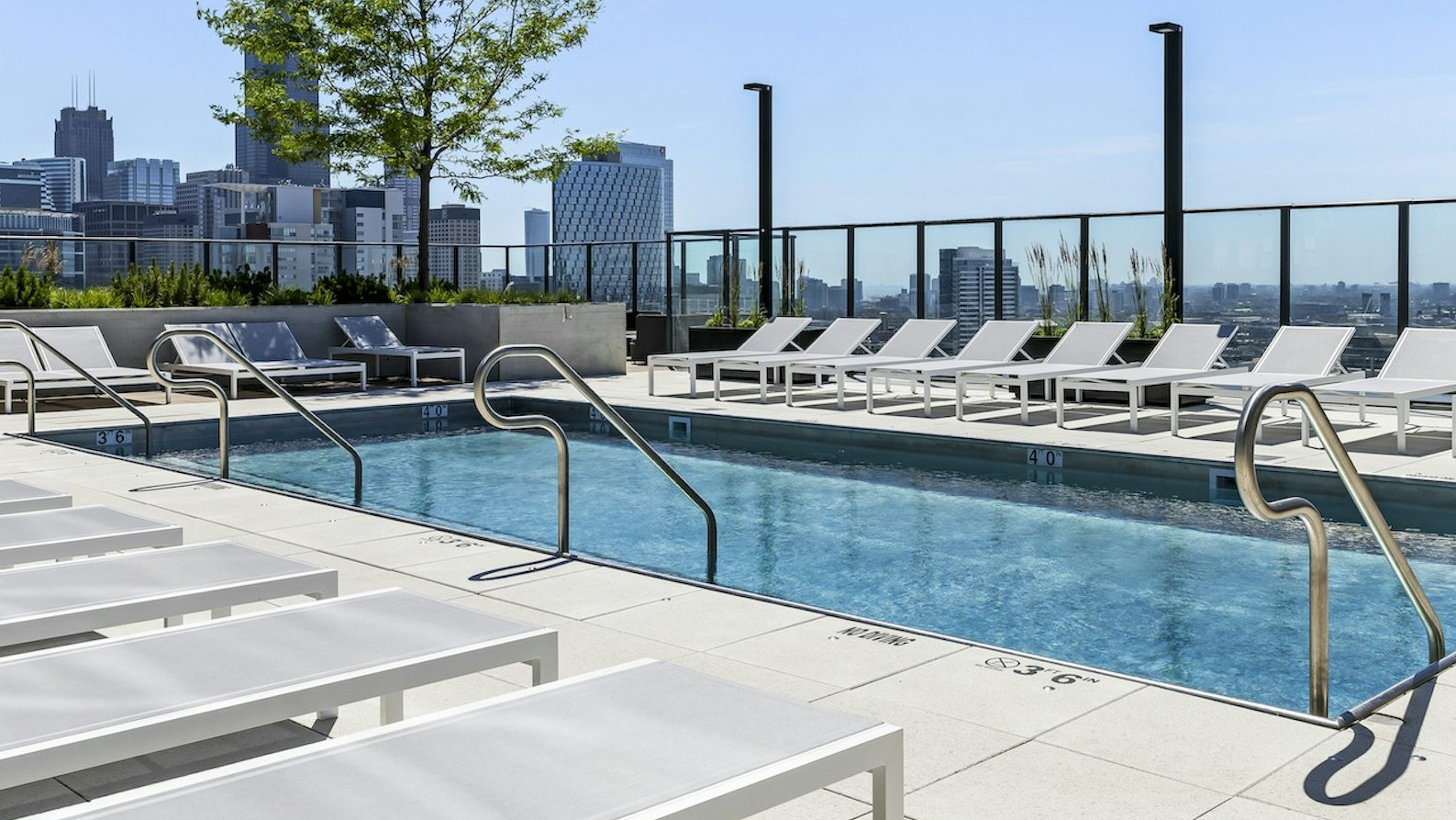 Modern rooftop swimming pool surrounded by lounge chairs, offering an impressive Chicago skyline backdrop under a sunny sky at The Dylan