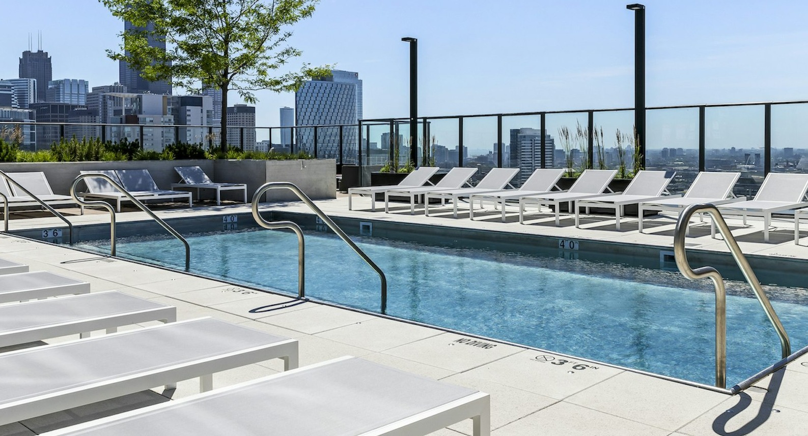 Modern rooftop swimming pool surrounded by lounge chairs, offering an impressive Chicago skyline backdrop under a sunny sky at The Dylan