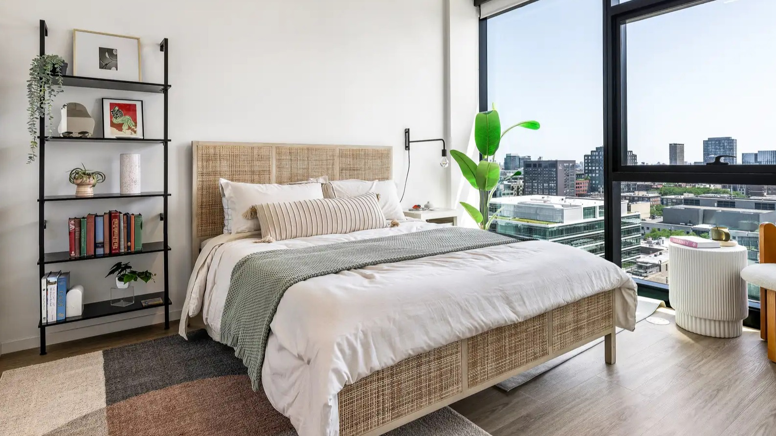 Modern apartment bedroom at The Elizabeth Chicago, featuring a comfortable bed, stylish shelving, and large windows with city views