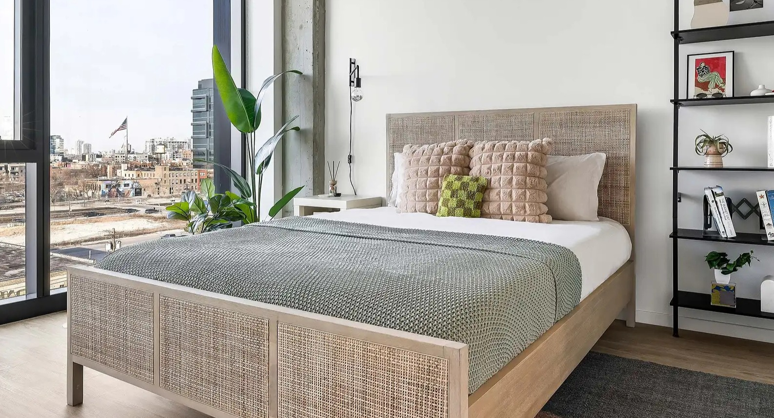 Bright apartment bedroom at The Elizabeth Chicago, featuring a natural wood bed frame, stylish decor, and expansive urban views