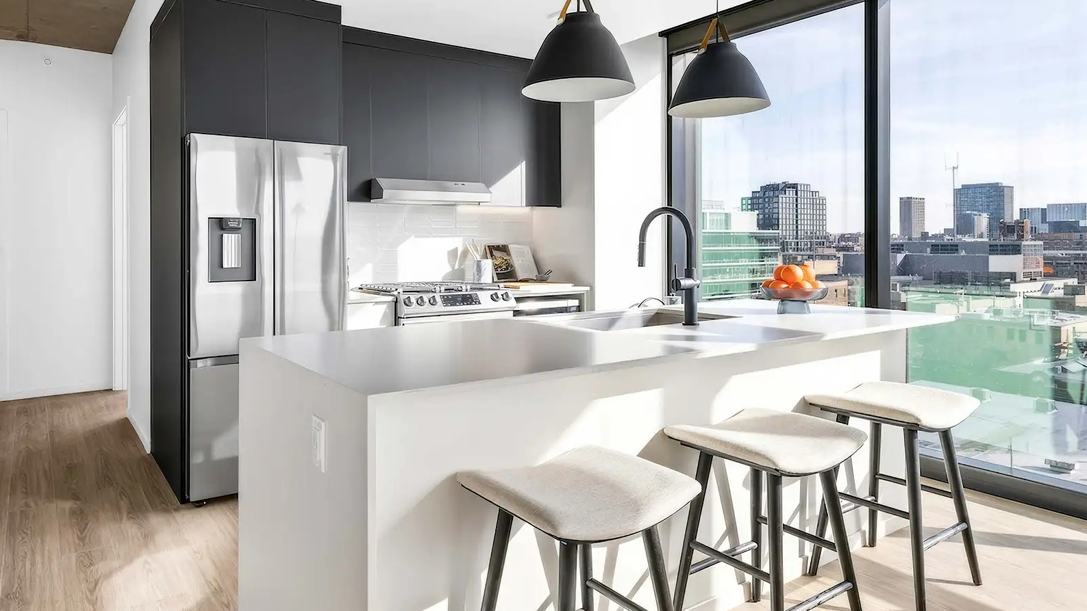Sleek apartment kitchen at The Elizabeth Chicago, featuring a white island with bar seating, modern appliances, and impressive city views
