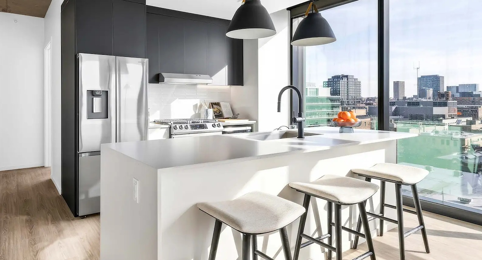 Sleek apartment kitchen at The Elizabeth Chicago, featuring a white island with bar seating, modern appliances, and impressive city views