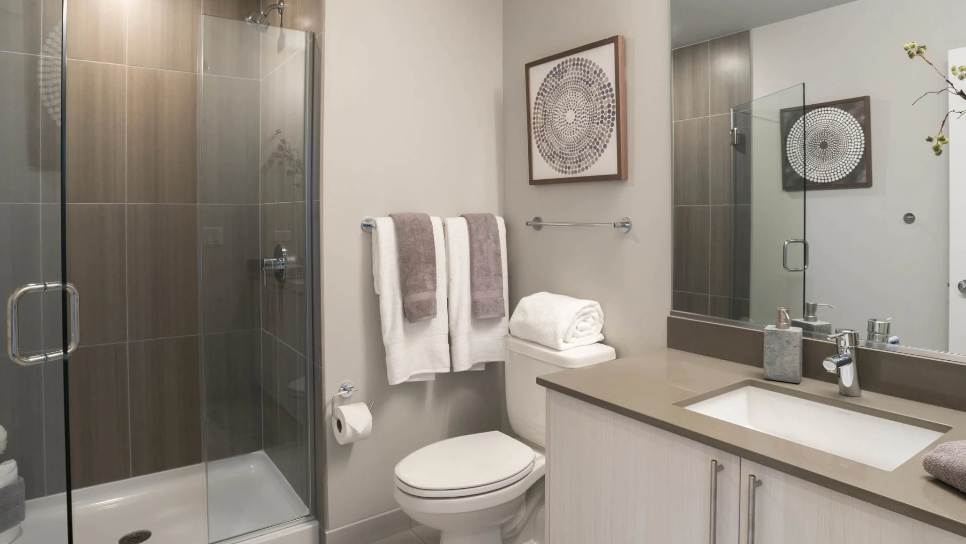 Modern bathroom featuring a spacious walk-in shower with stylish brown tiles, a large vanity, and elegant decor at The Elle in Chicago