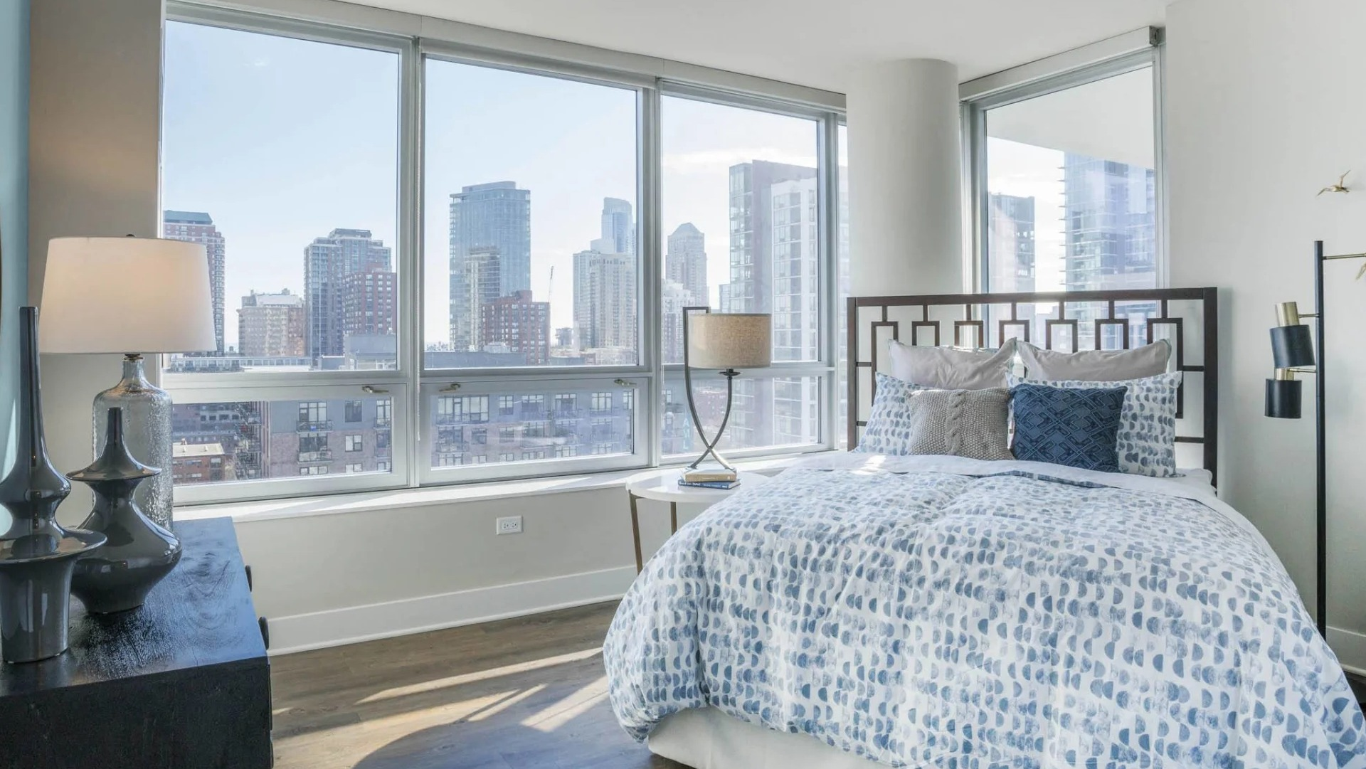 Bright bedroom with a comfortable bed, large windows offering panoramic city views, and modern decor at The Elle apartments in Chicago