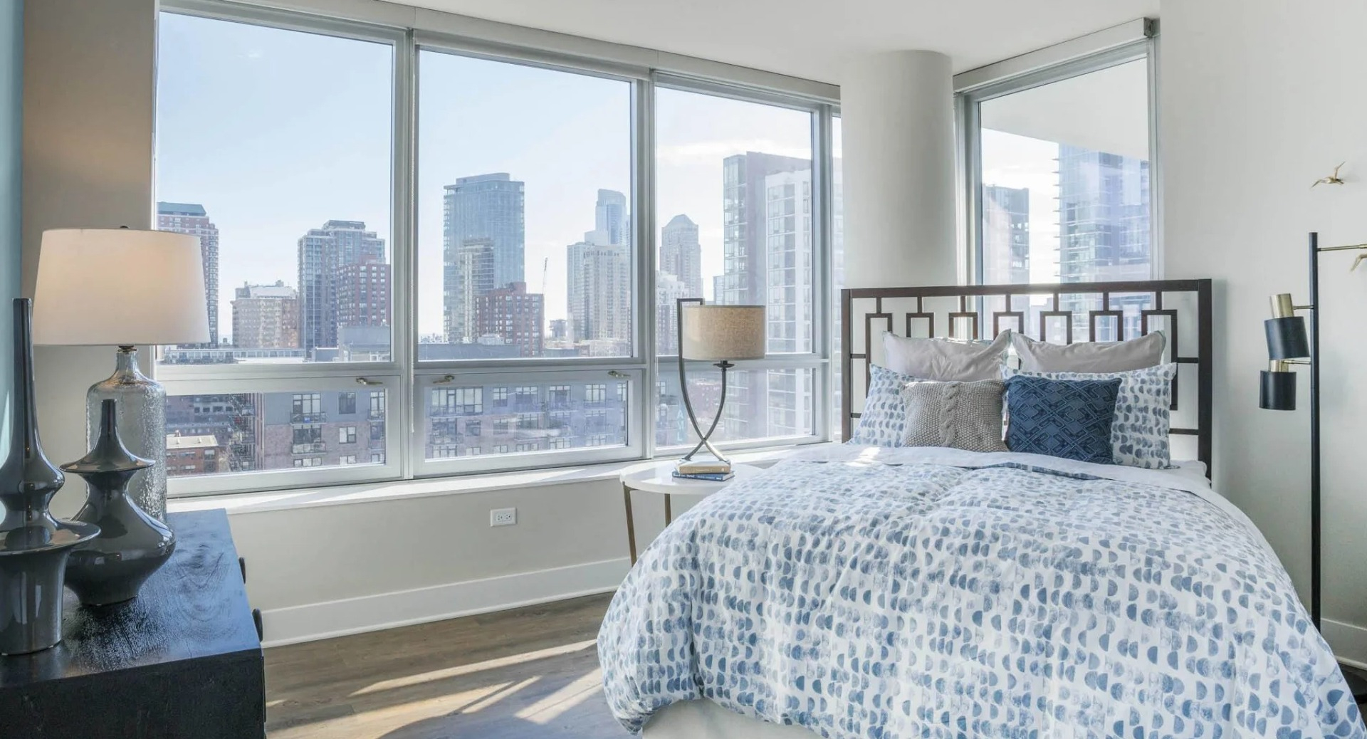 Bright bedroom with a comfortable bed, large windows offering panoramic city views, and modern decor at The Elle apartments in Chicago