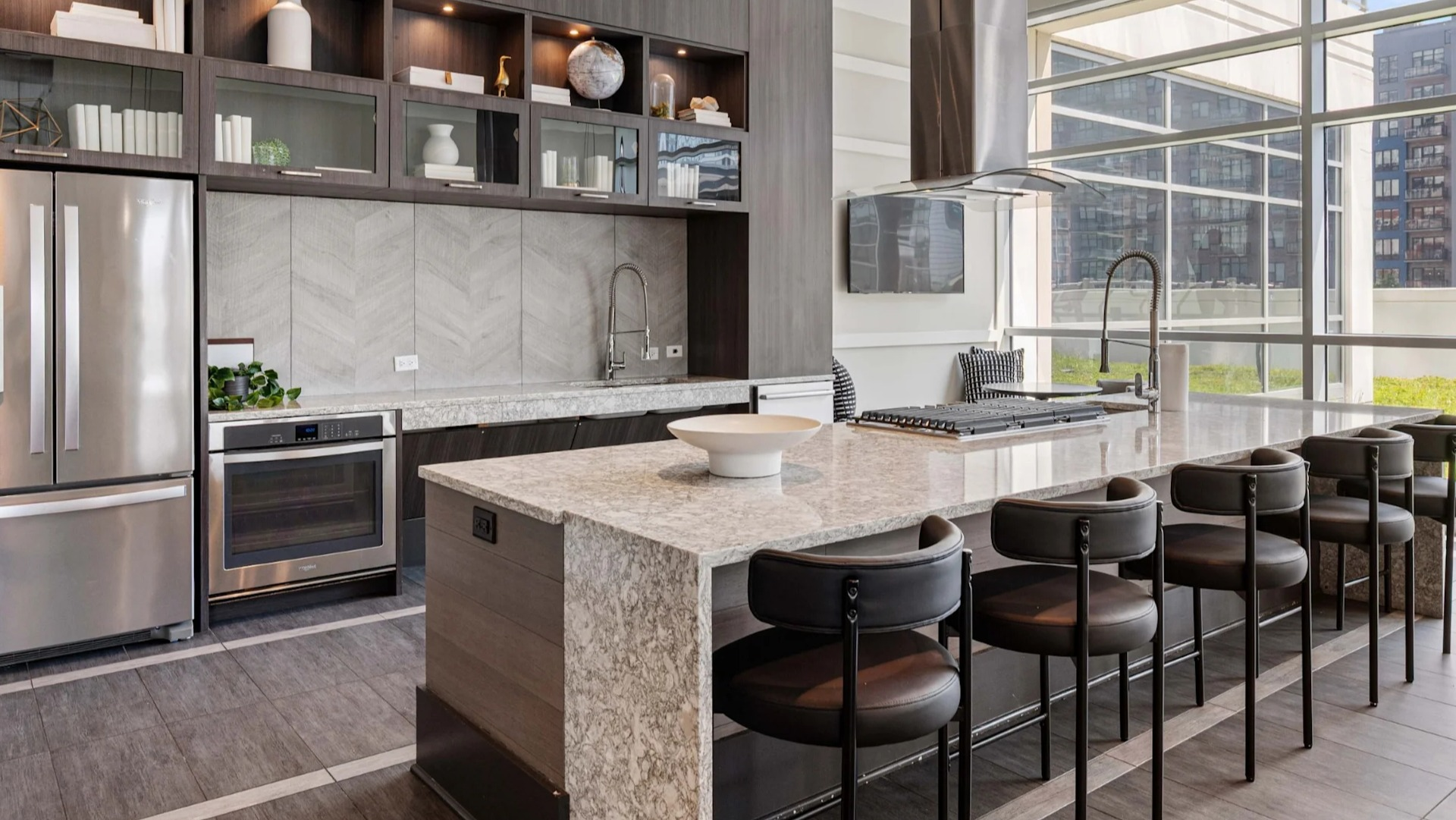 Sleek gourmet community kitchen with dark wood cabinetry, stainless steel appliances, a large island with bar seating, and ample natural light at The Elle in Chicago