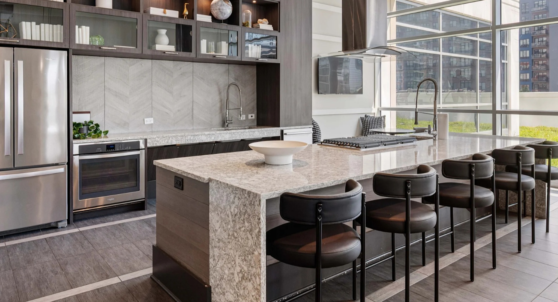 Sleek gourmet community kitchen with dark wood cabinetry, stainless steel appliances, a large island with bar seating, and ample natural light at The Elle in Chicago