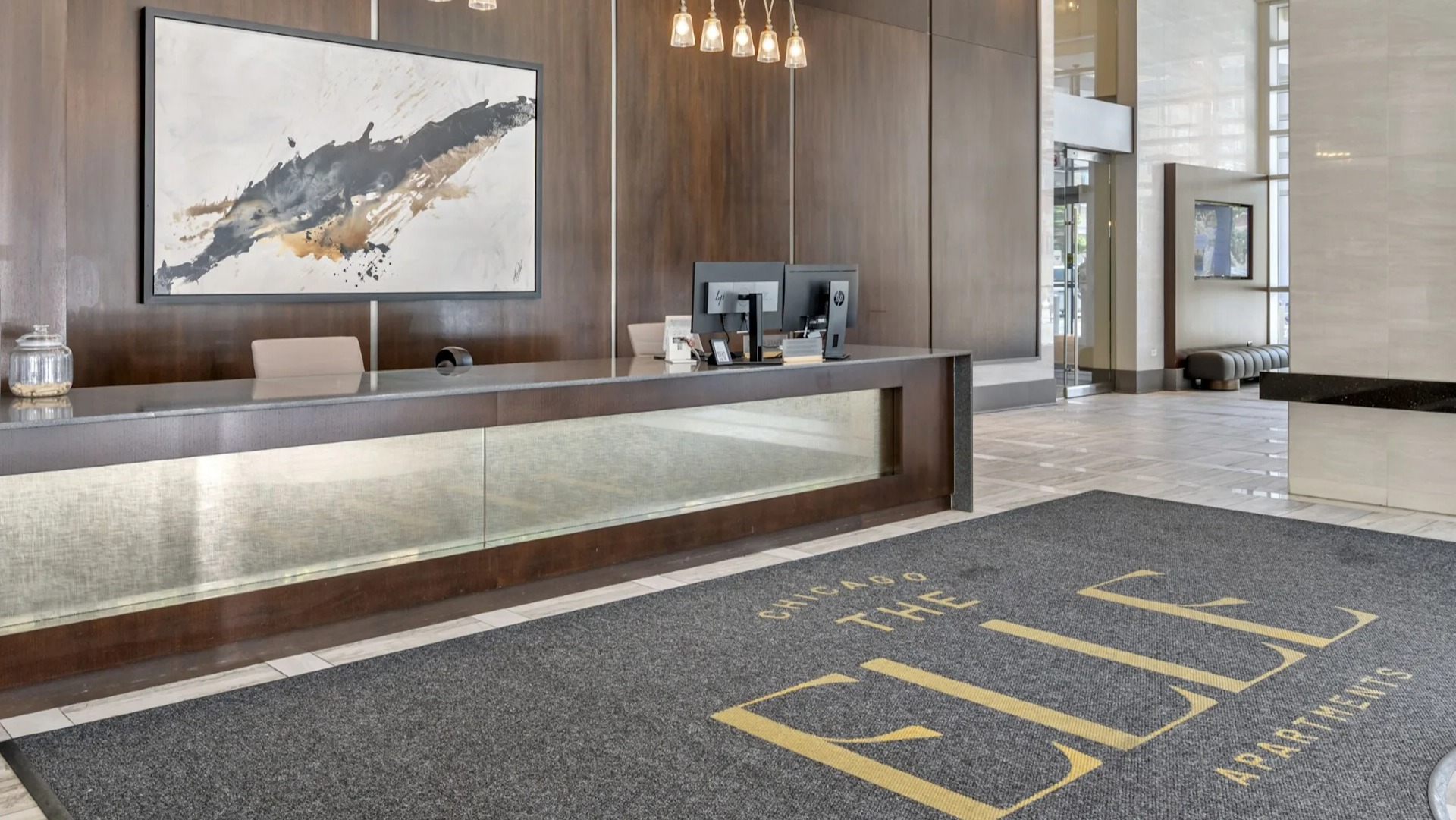 Elegant main lobby and reception area with a stylish desk, modern lighting, and a welcome mat for The Elle Apartments in Chicago