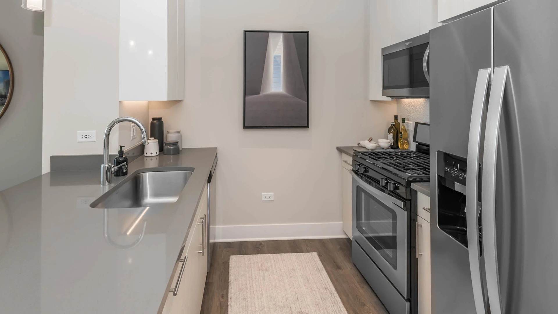 Contemporary apartment kitchen with sleek grey countertops, white cabinetry, stainless steel appliances, and track lighting at The Elle in Chicago