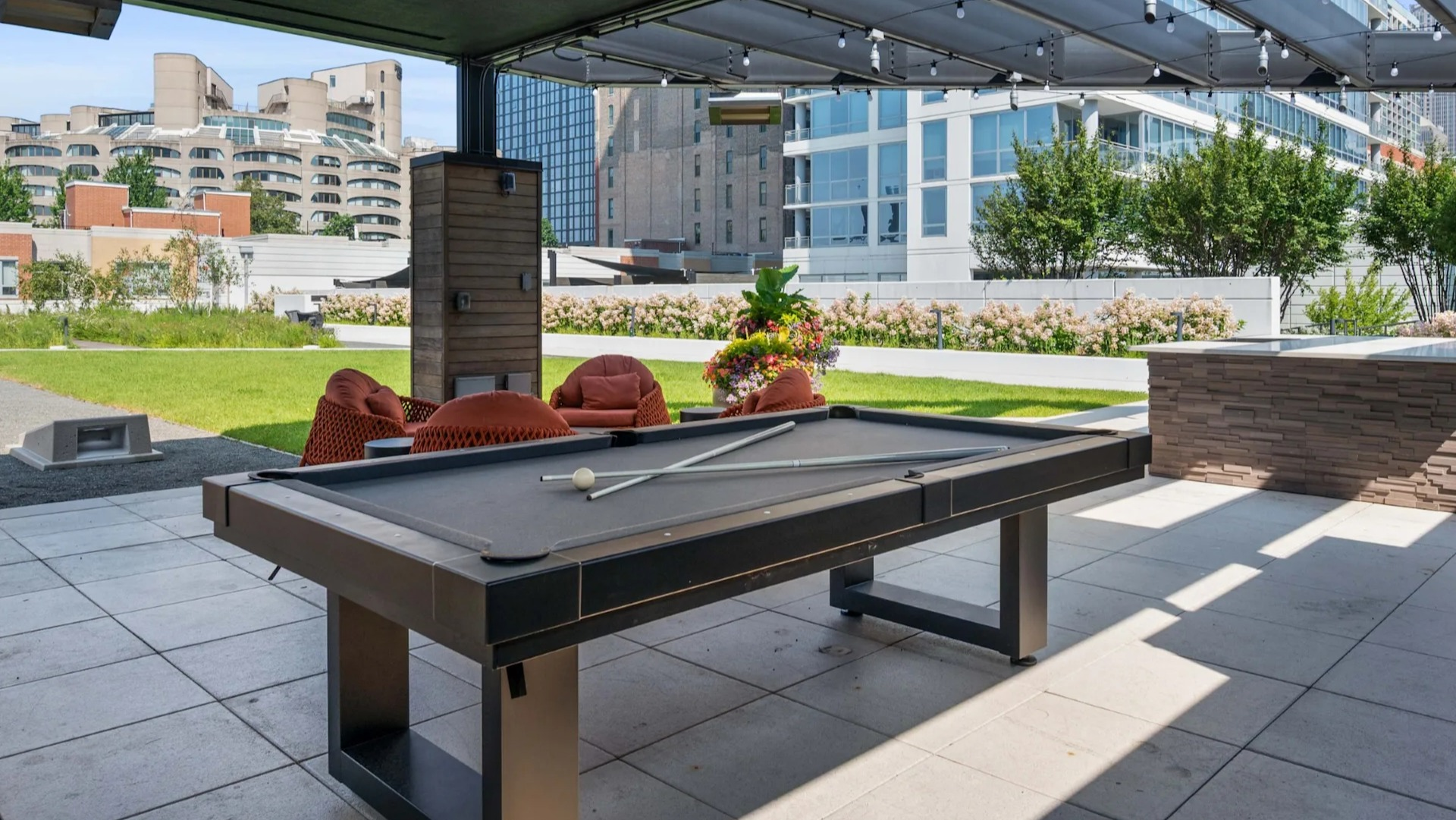 Expansive outdoor patio featuring a billiards table, comfortable seating, and city views under a shaded pergola at The Elle in Chicago
