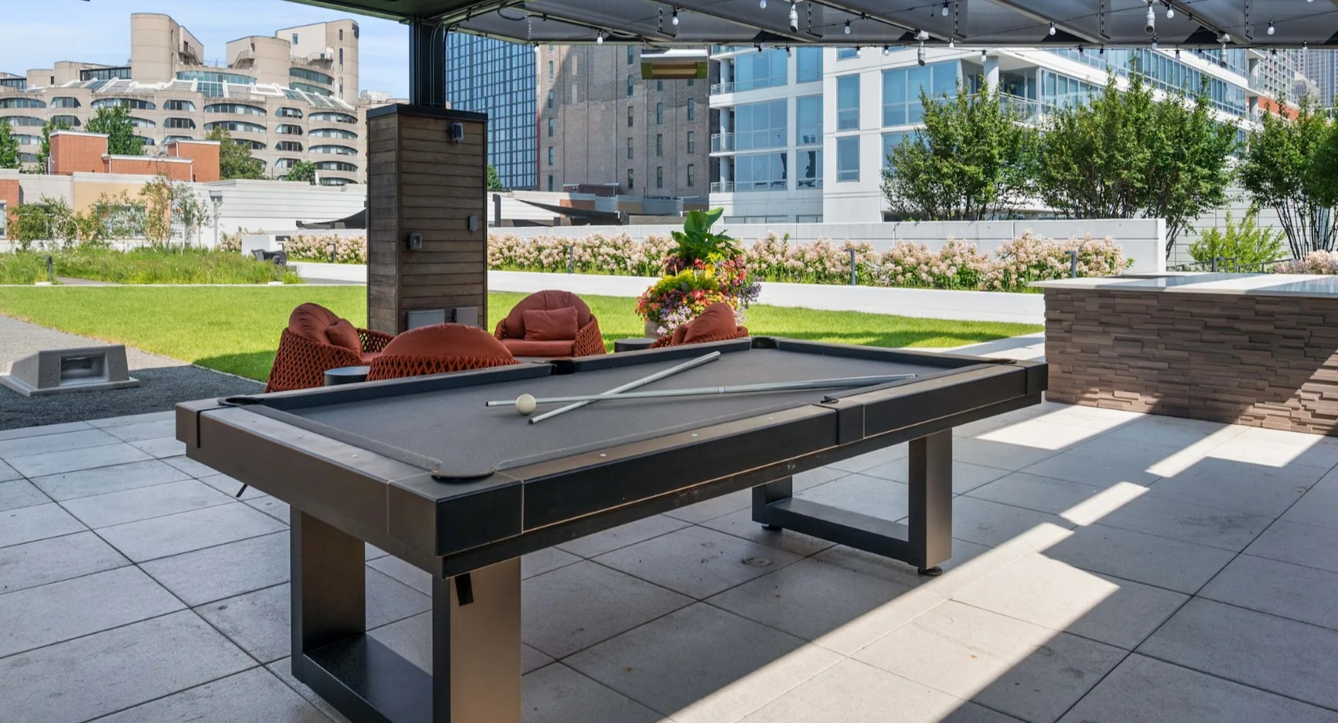 Expansive outdoor patio featuring a billiards table, comfortable seating, and city views under a shaded pergola at The Elle in Chicago