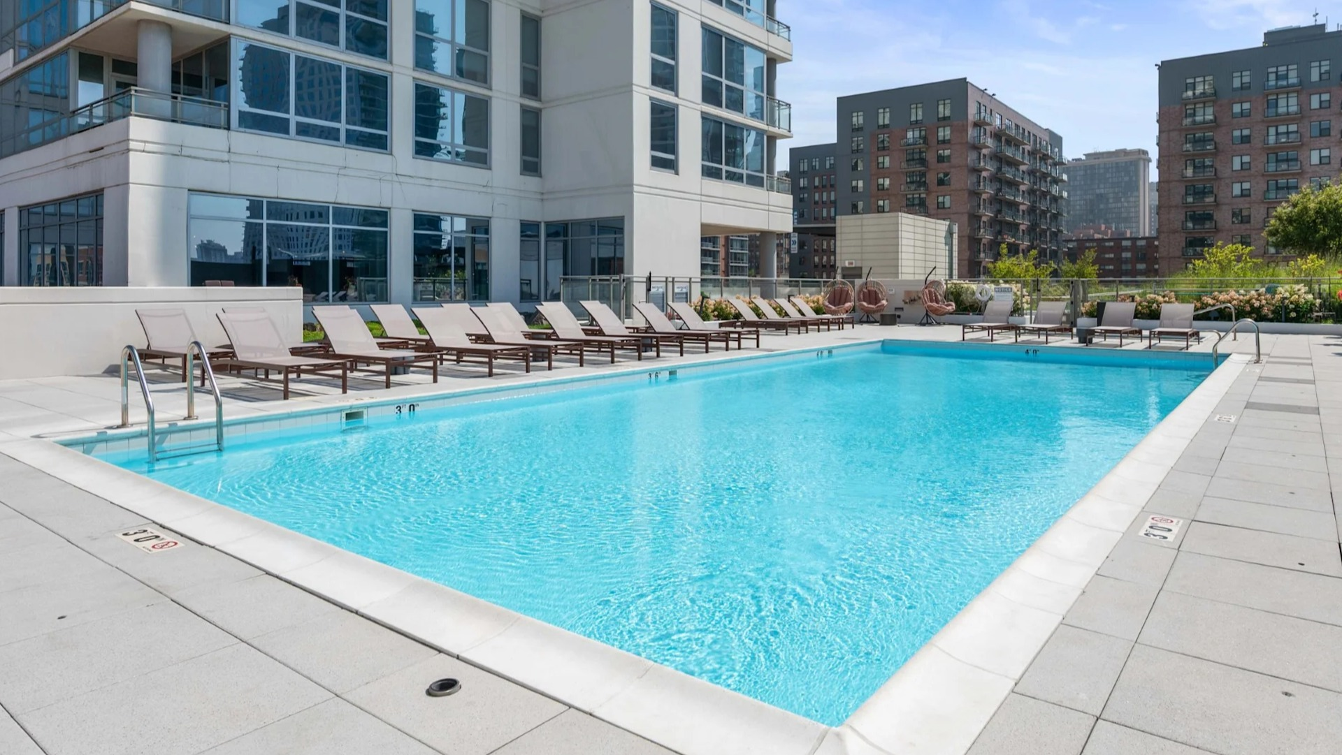 Inviting outdoor swimming pool with lounge chairs, offering beautiful city views and modern building architecture at The Elle in Chicago