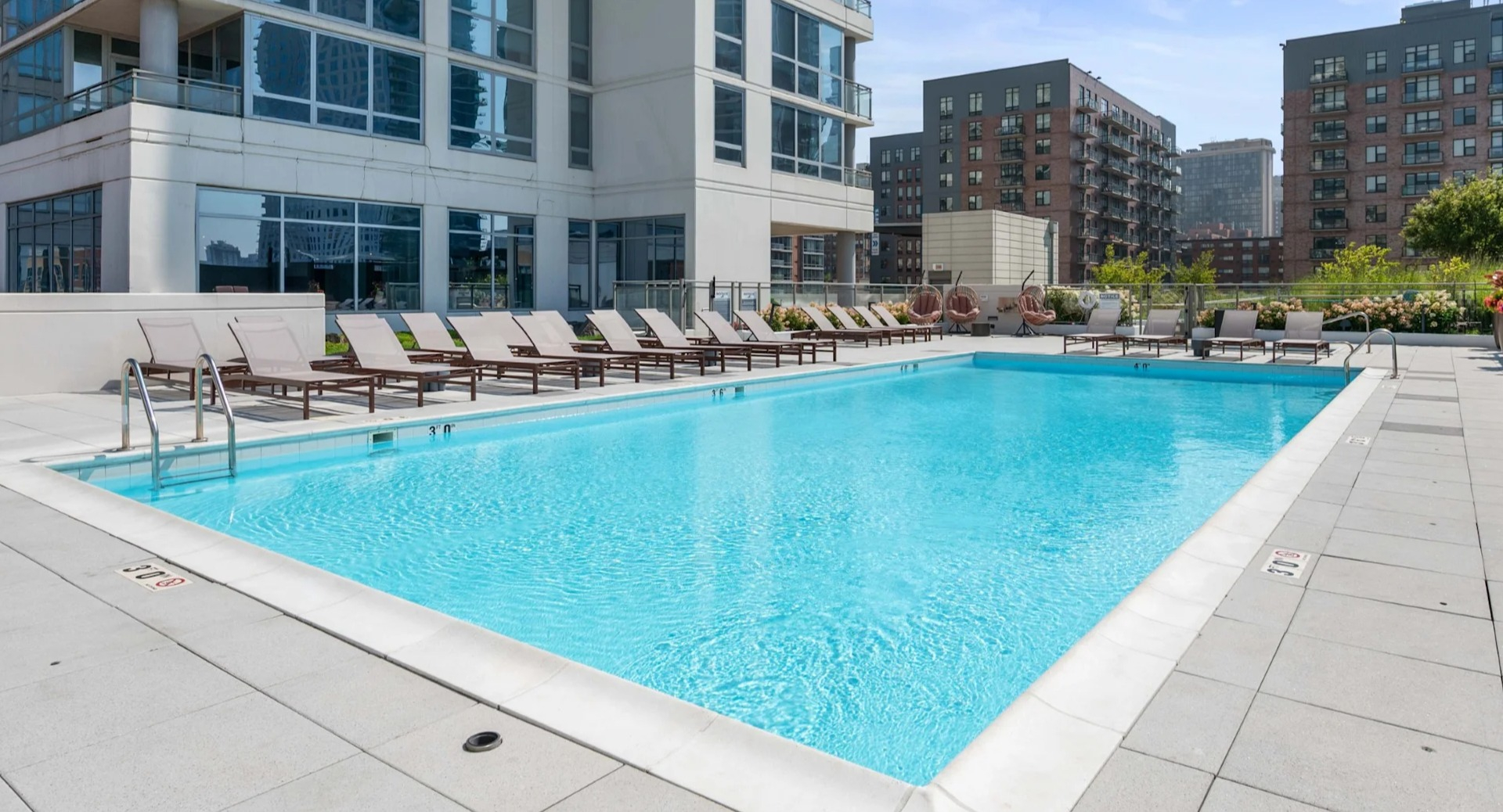 Inviting outdoor swimming pool with lounge chairs, offering beautiful city views and modern building architecture at The Elle in Chicago