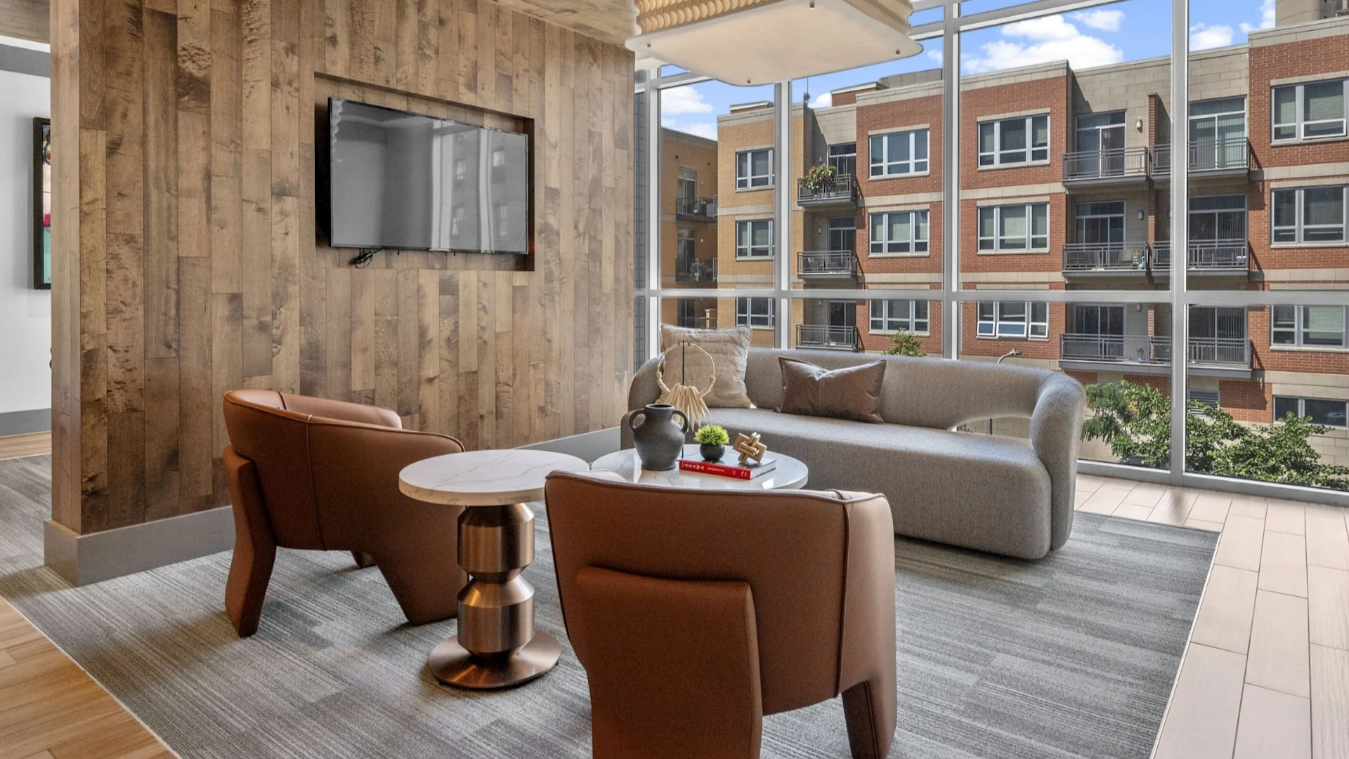 Inviting resident lounge with comfortable seating, a television, and large windows overlooking city buildings at The Elle in Chicago