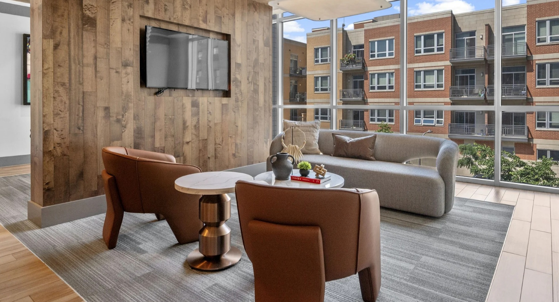 Inviting resident lounge with comfortable seating, a television, and large windows overlooking city buildings at The Elle in Chicago