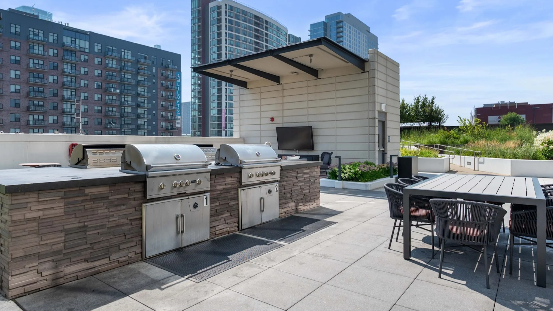 Spacious rooftop area with built-in BBQ grills, outdoor dining tables, and cityscape views at The Elle apartments in Chicago