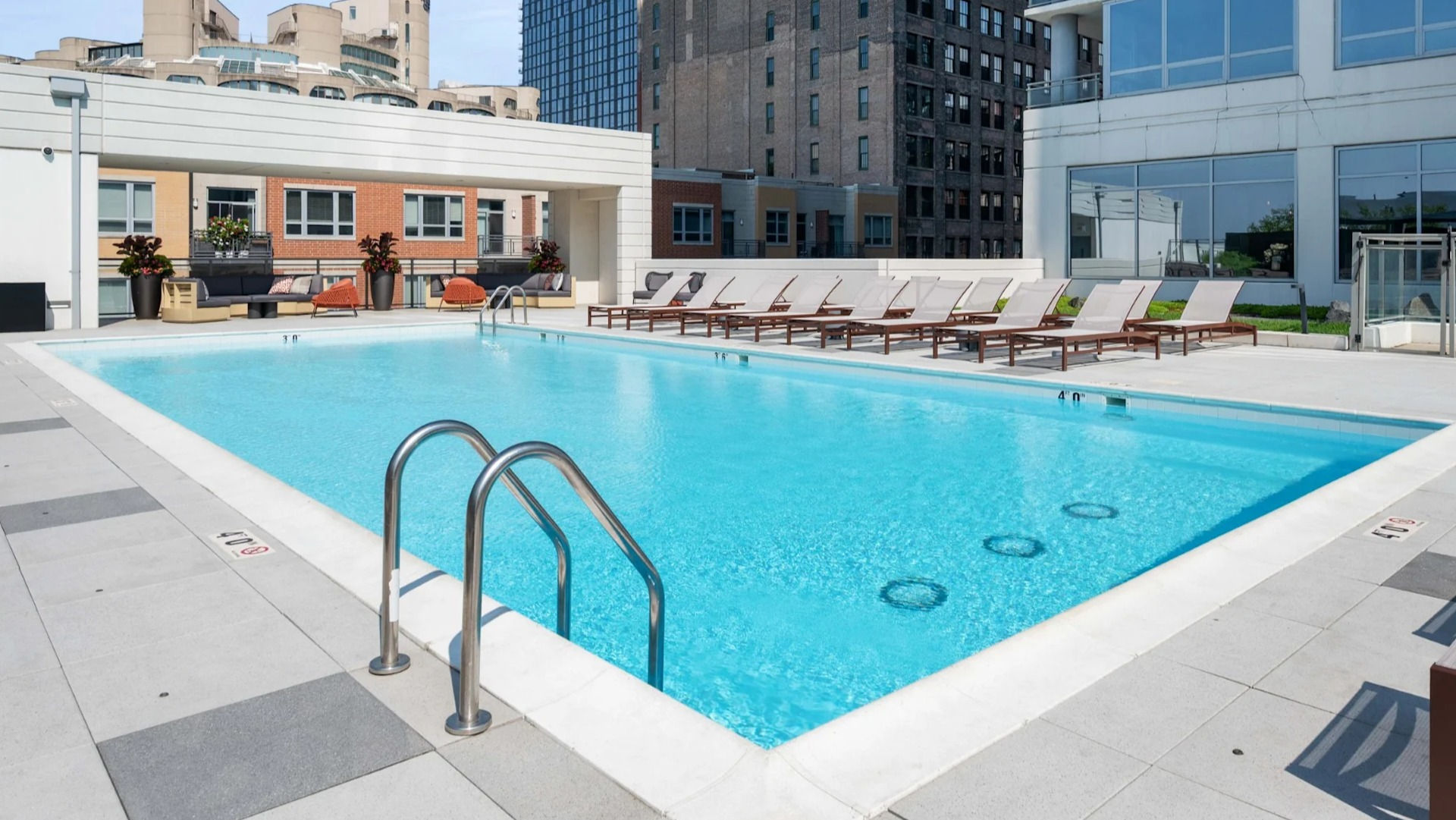 Expansive rooftop swimming pool surrounded by comfortable lounge seating, featuring a modern design and city backdrop at The Elle in Chicago