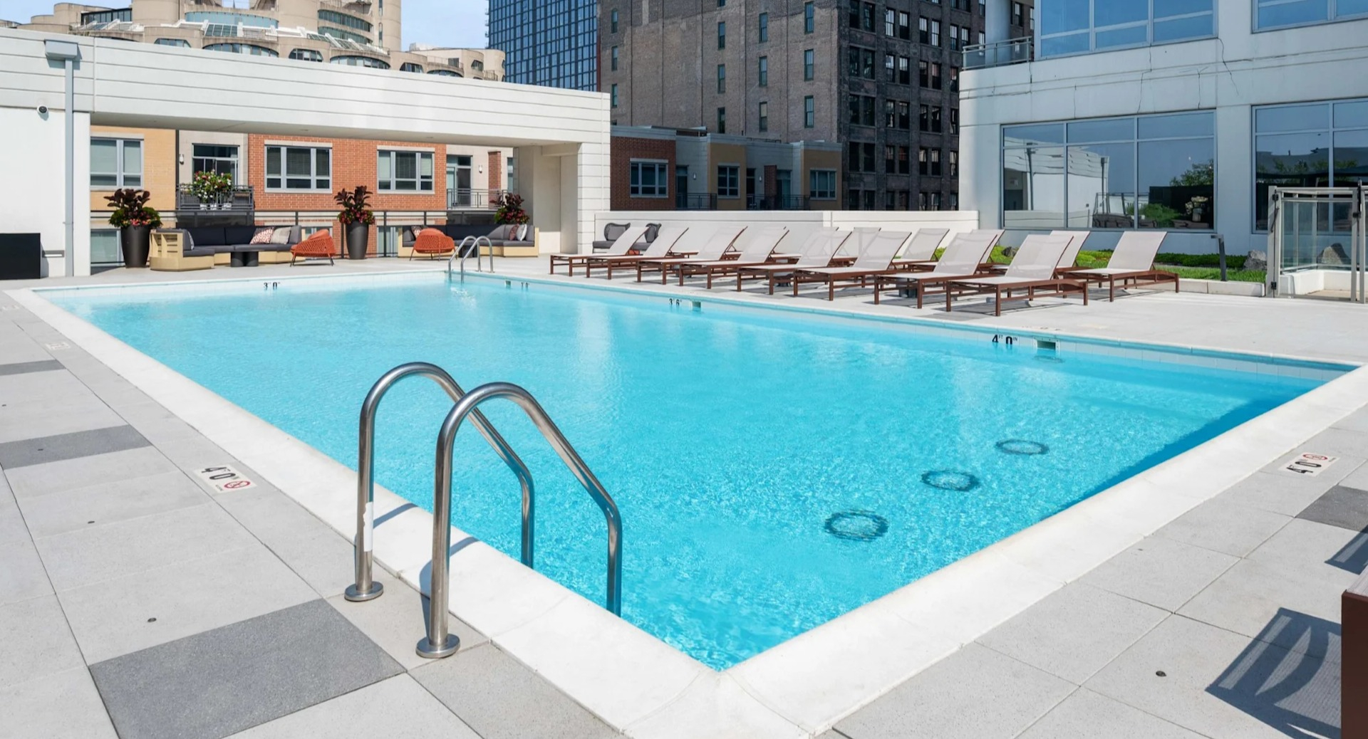 Expansive rooftop swimming pool surrounded by comfortable lounge seating, featuring a modern design and city backdrop at The Elle in Chicago