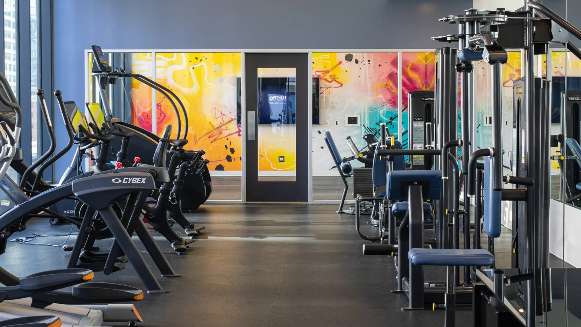 Expansive gym featuring a wide range of cardio and strength training equipment, with dynamic wall art at The Gallery on Wells in Chicago