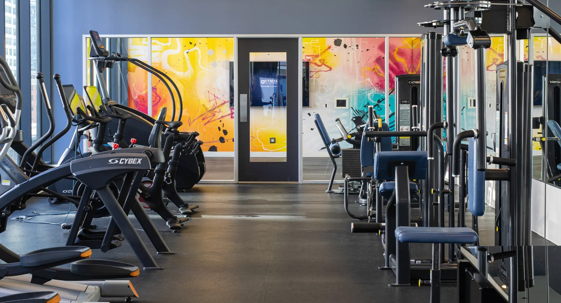 Expansive gym featuring a wide range of cardio and strength training equipment, with dynamic wall art at The Gallery on Wells in Chicago