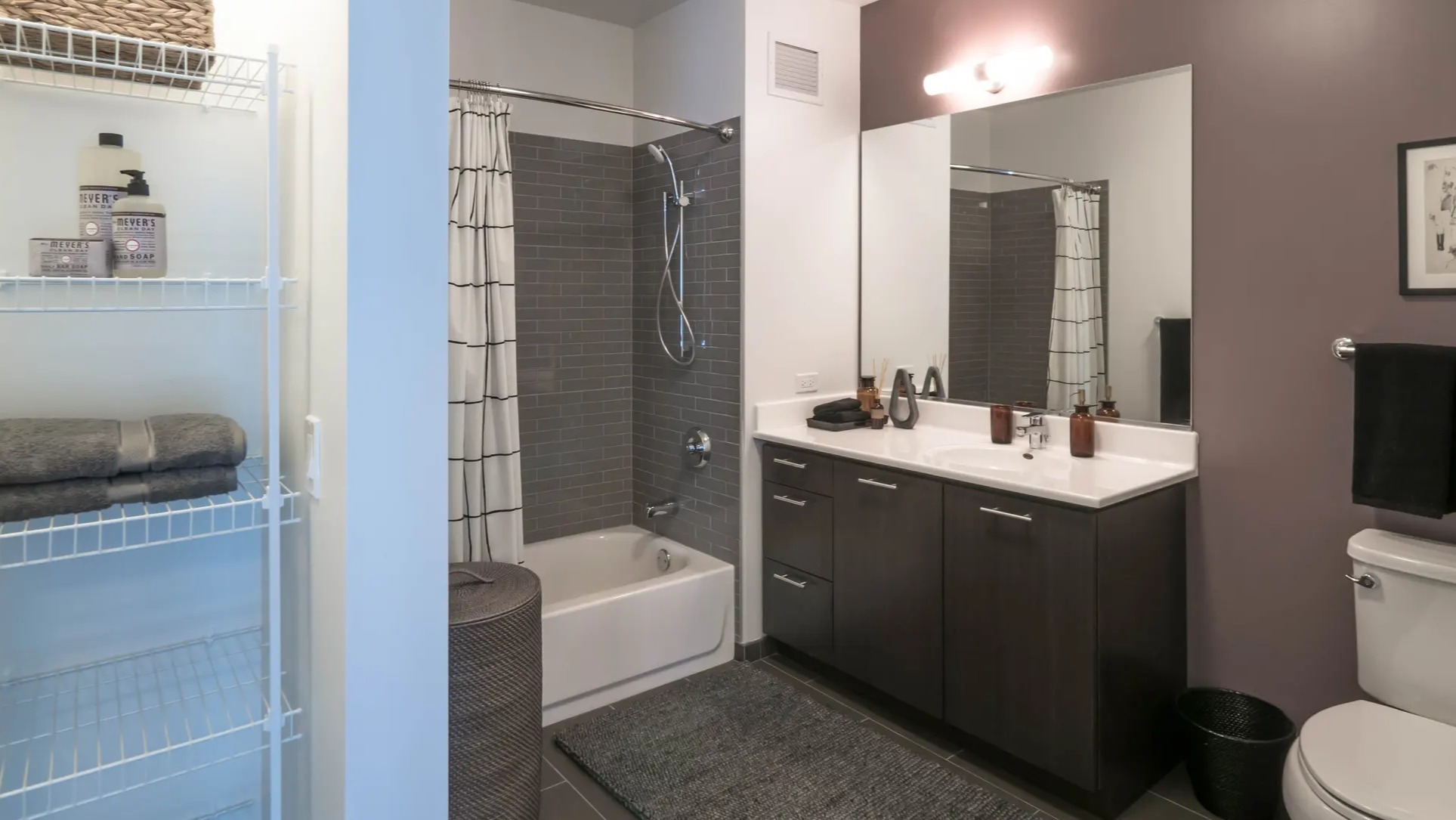 Modern bathroom with a bathtub, subway tiled shower, dark vanity, and open shelving for storage at The Gallery on Wells in Chicago