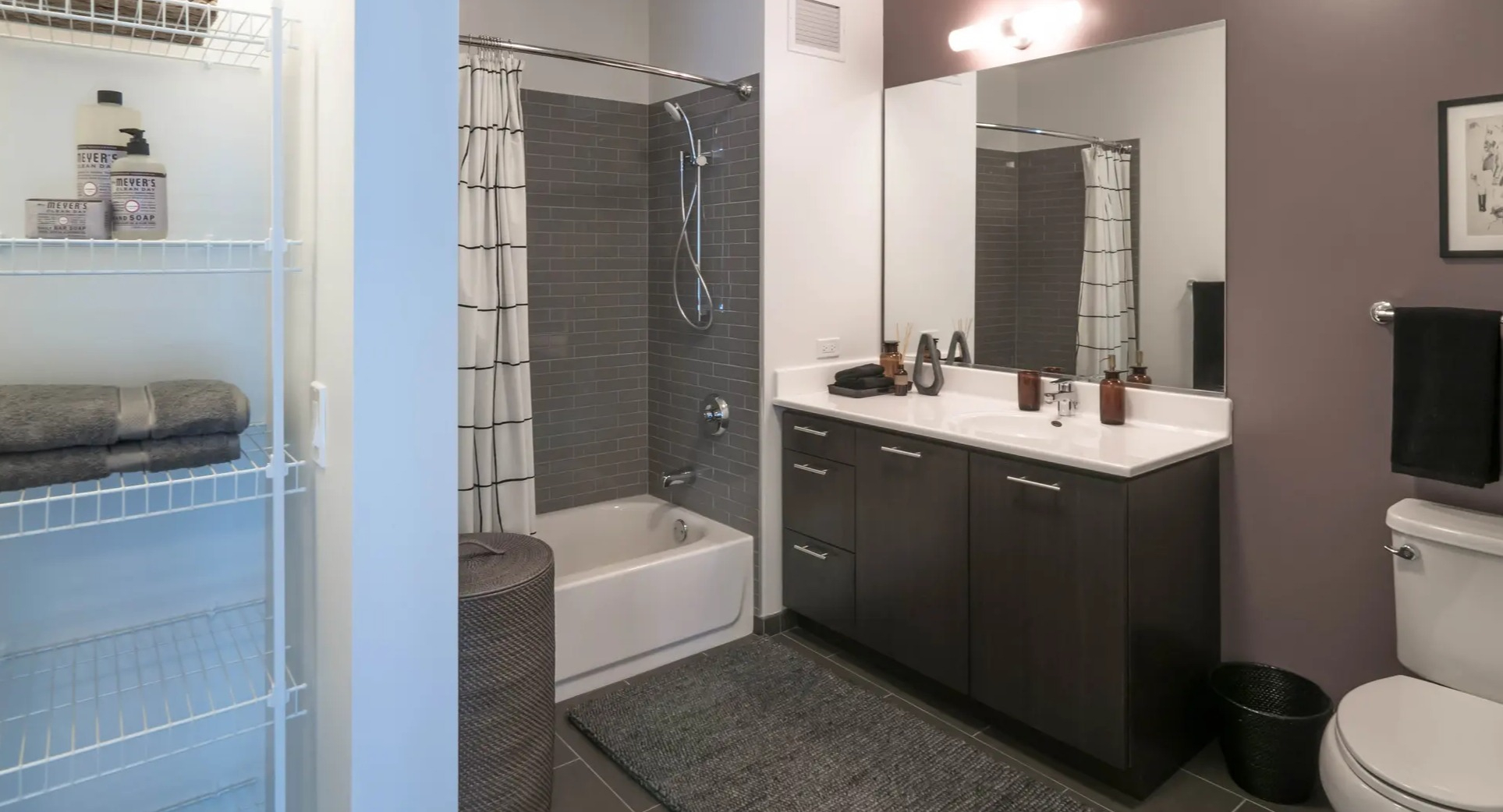 Modern bathroom with a bathtub, subway tiled shower, dark vanity, and open shelving for storage at The Gallery on Wells in Chicago