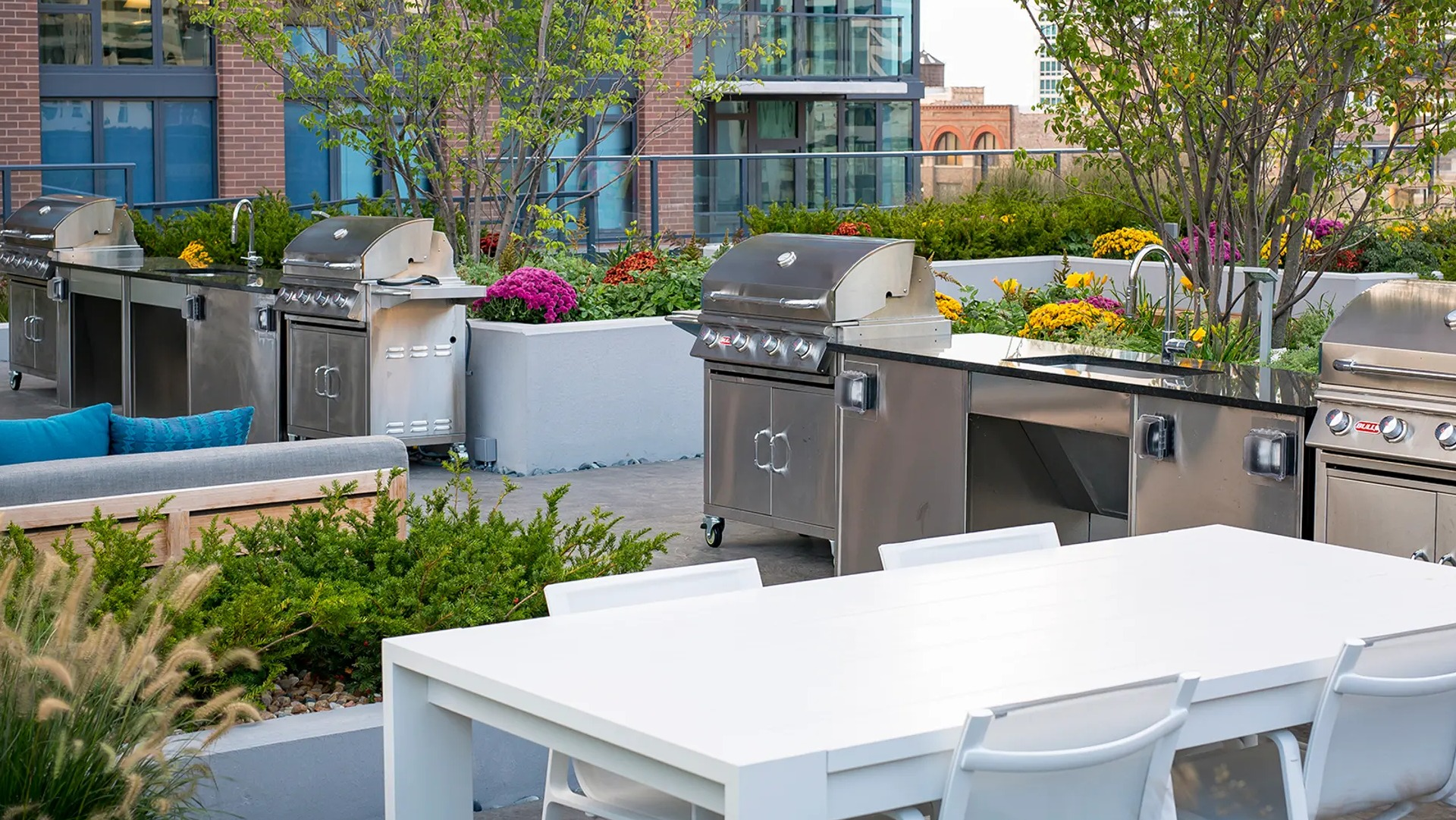 Spacious outdoor grilling area with multiple stainless steel grills, a large dining table, and lush landscaping at The Gallery on Wells in Chicago