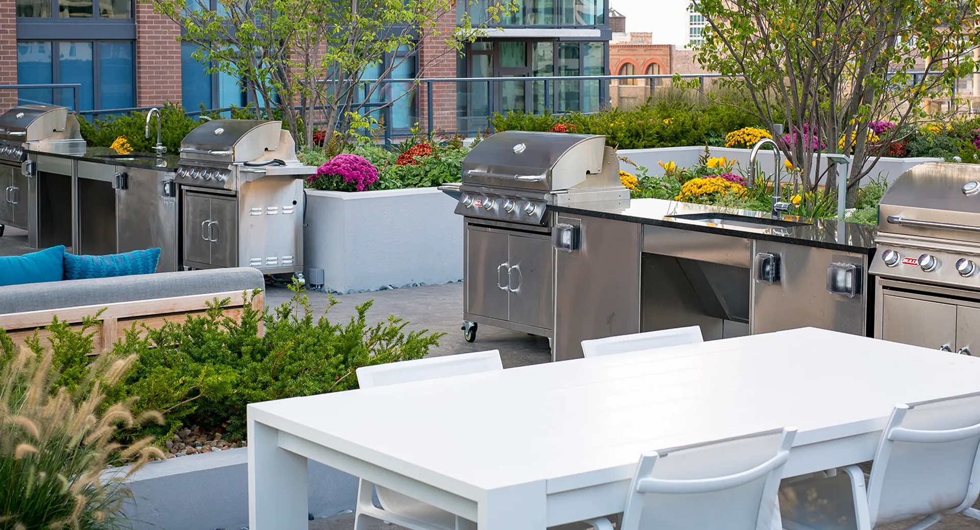 Spacious outdoor grilling area with multiple stainless steel grills, a large dining table, and lush landscaping at The Gallery on Wells in Chicago