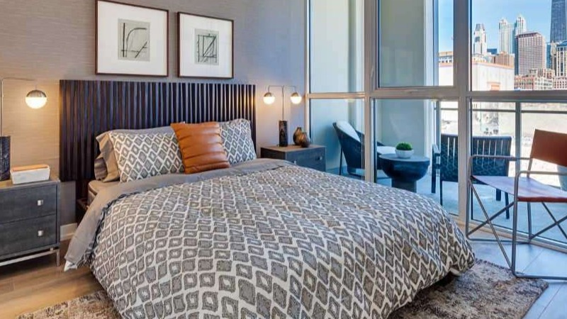 Chic apartment bedroom at The Hudson in Chicago, featuring a stylish bed, modern decor, and a private balcony with city skyline views