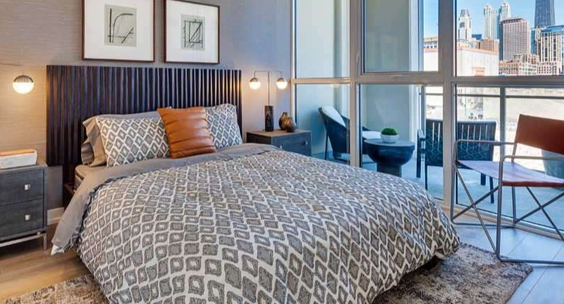 Chic apartment bedroom at The Hudson in Chicago, featuring a stylish bed, modern decor, and a private balcony with city skyline views