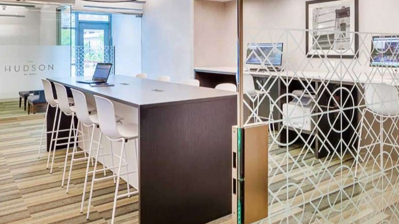 Modern business center at The Hudson in Chicago, featuring communal tables, private workstations, and ample natural light