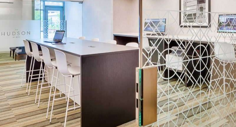 Modern business center at The Hudson in Chicago, featuring communal tables, private workstations, and ample natural light