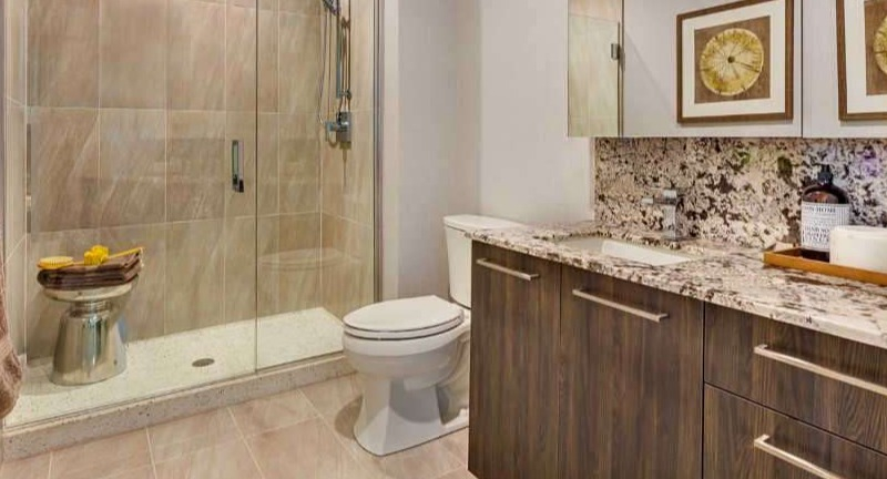 Modern apartment bathroom at The Hudson in Chicago, featuring a sleek vanity with granite, large mirror, and a spacious walk-in shower